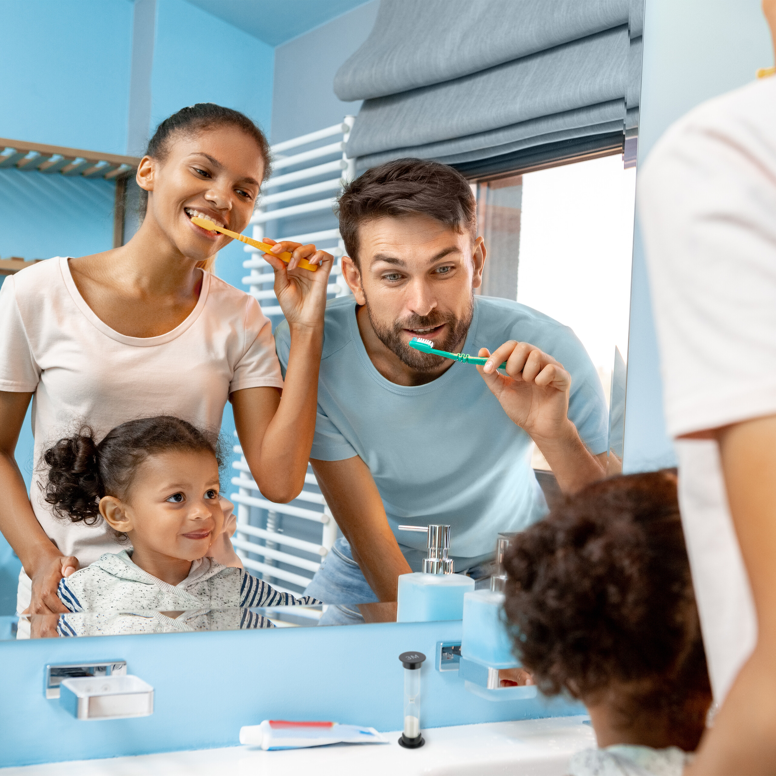 Eine Familie mit einem Kind putzt sich gemeinsam im Badezimmer vor dem Spiegel die Zähne.