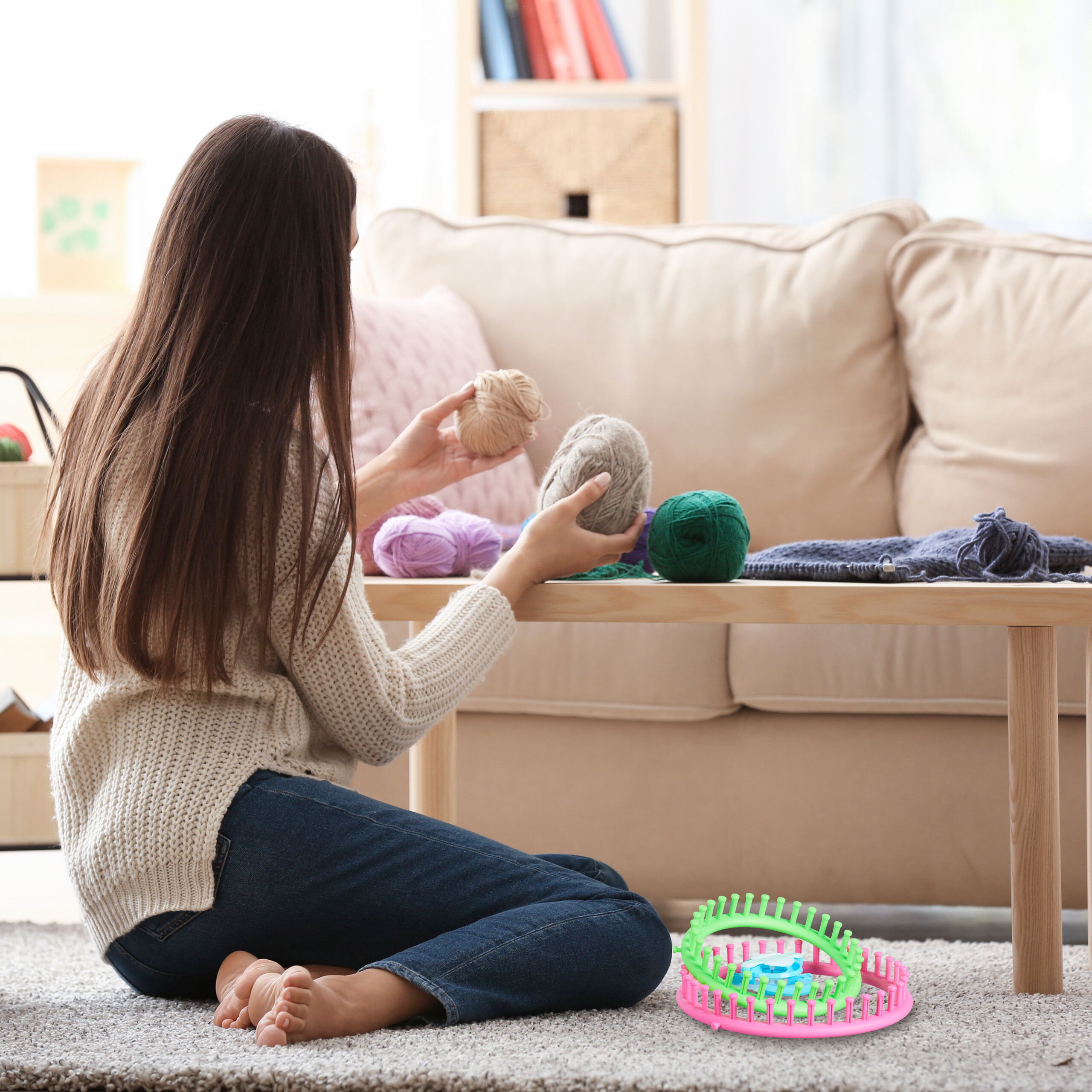 Eine Frau sitzt auf dem Boden vor einem Sofa und hält Wollknäuel in der Hand.