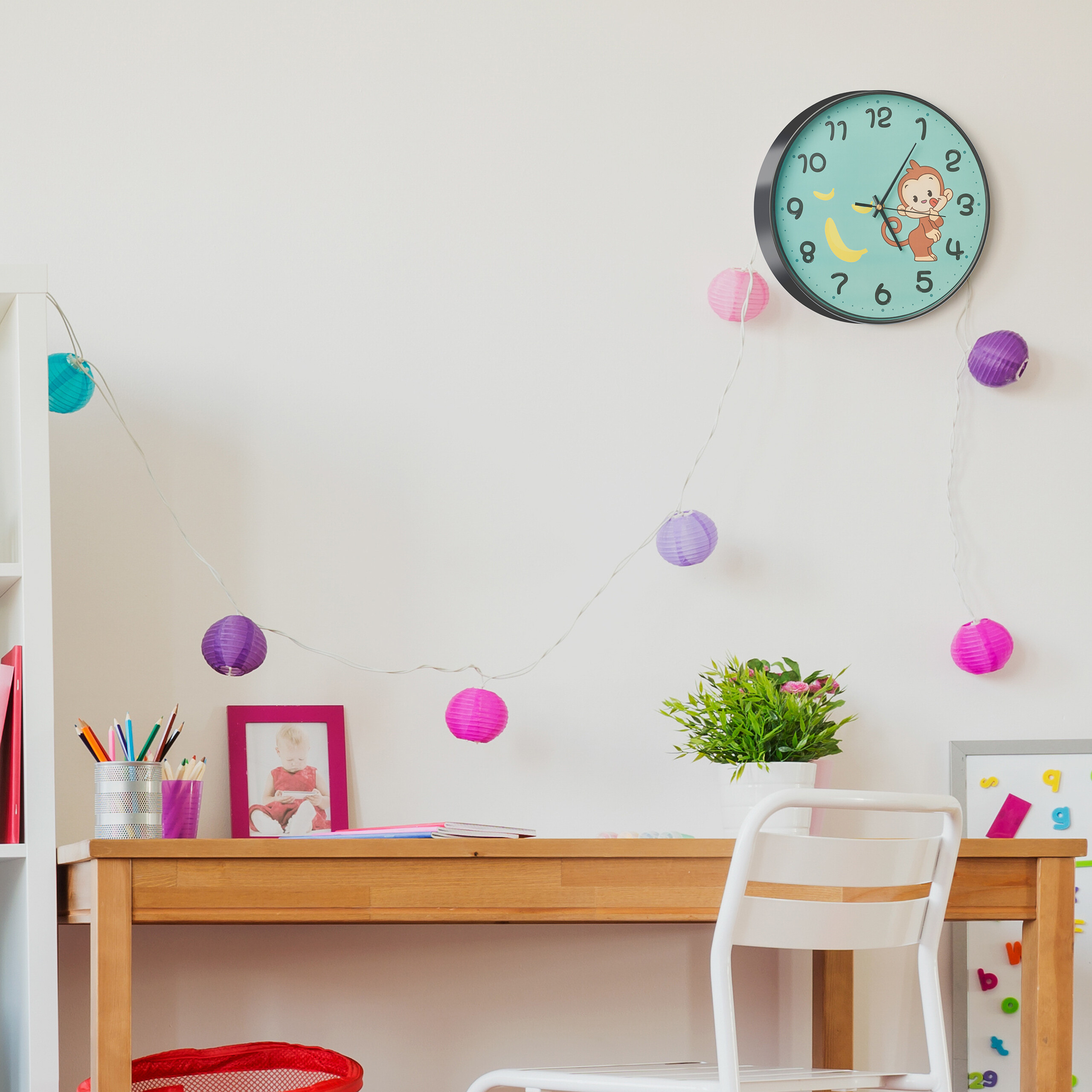 Ein Holztisch mit Stuhl, eine Uhr an der Wand, eine Lichterkette und bunte Dekorationen in einem Zimmer.