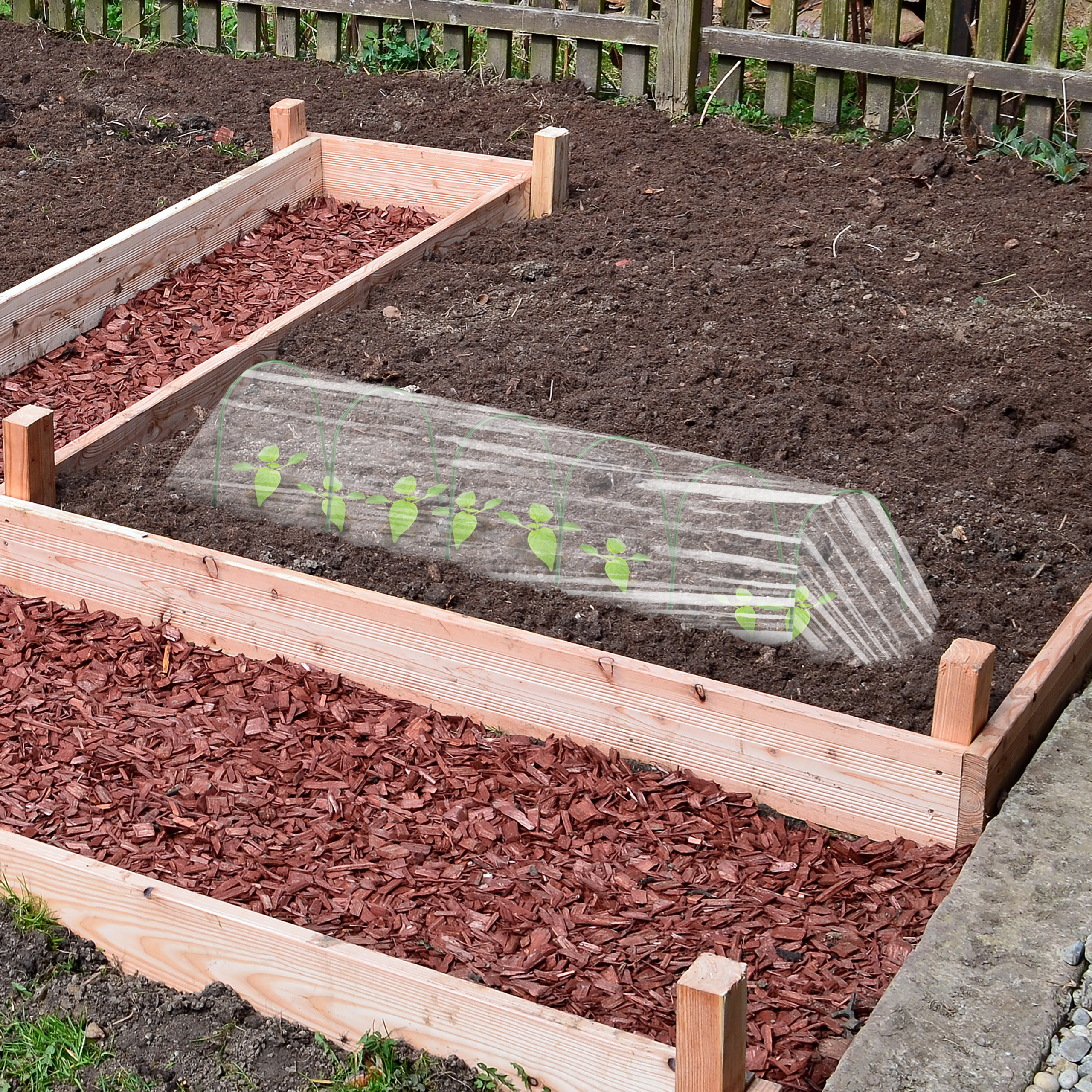 Hochbeete mit Rindenmulch und eine Mini-Gewächshausfolie über jungen Pflanzen.