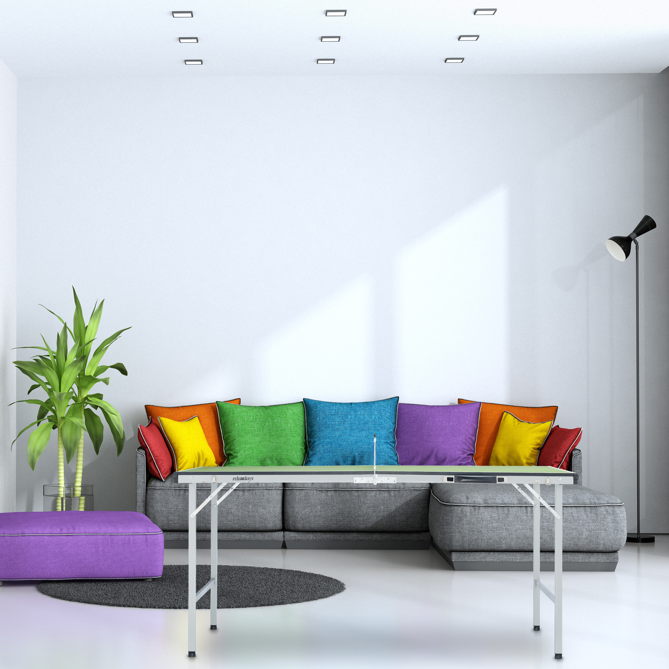 Ein graues Sofa mit bunten Kissen steht an einer weißen Wand, vorne ist ein Tischtennisspiel.