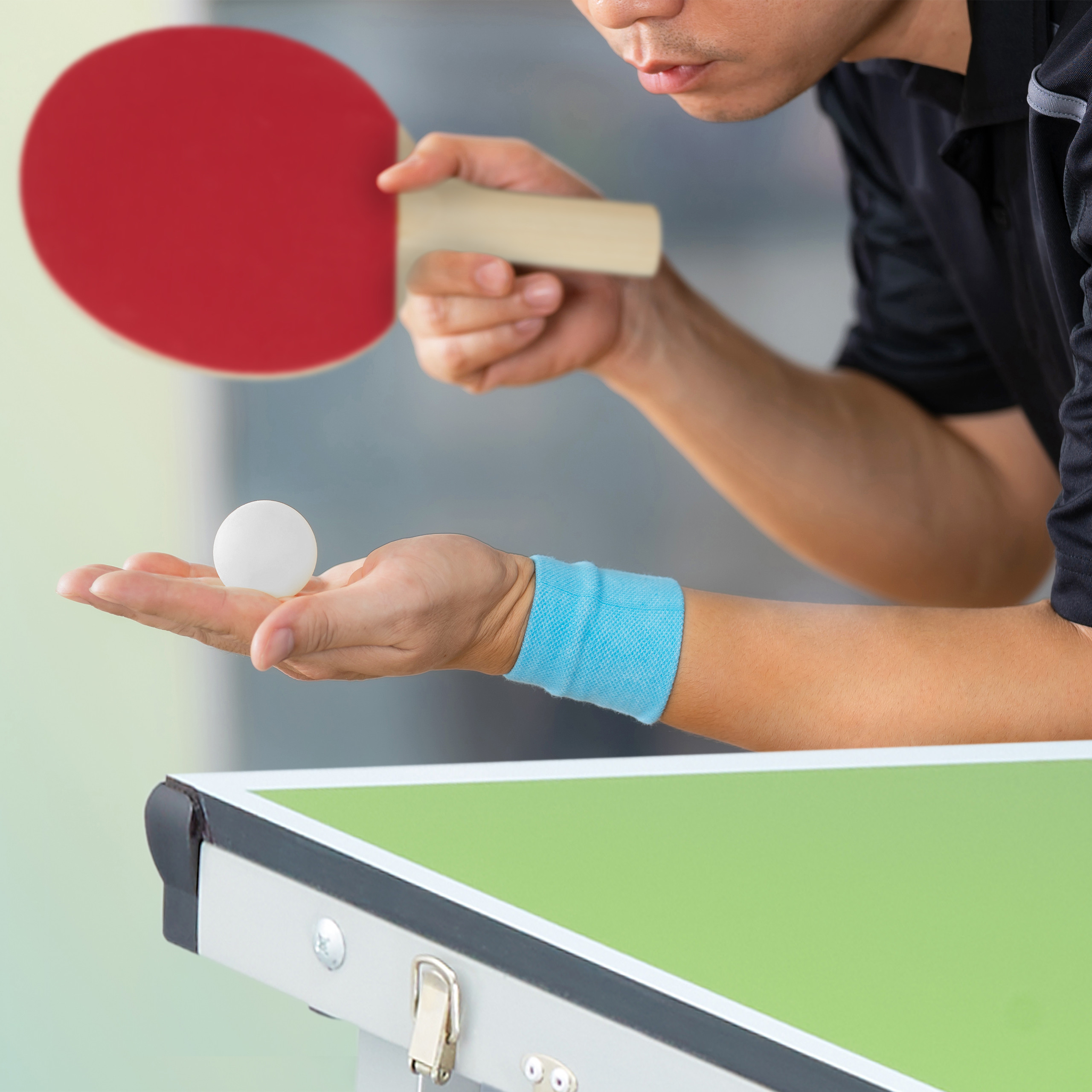 Ein Spieler hält einen weißen Tischtennisball auf offener Hand über einem grünen Tisch, mit einem roten Schläger.