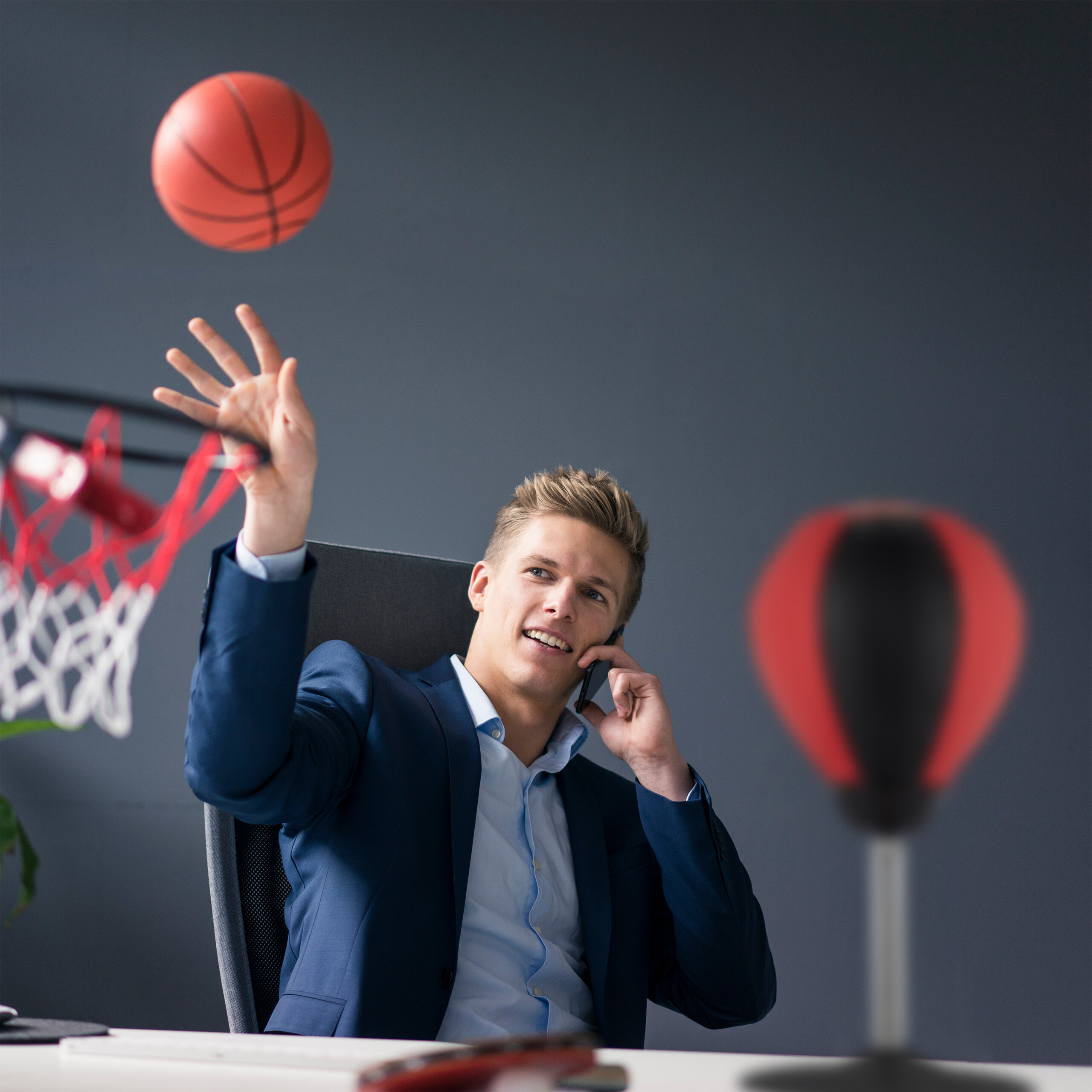 Geschäftsmann in Anzug telefoniert und wirft Basketball in einen Korb im Büro.