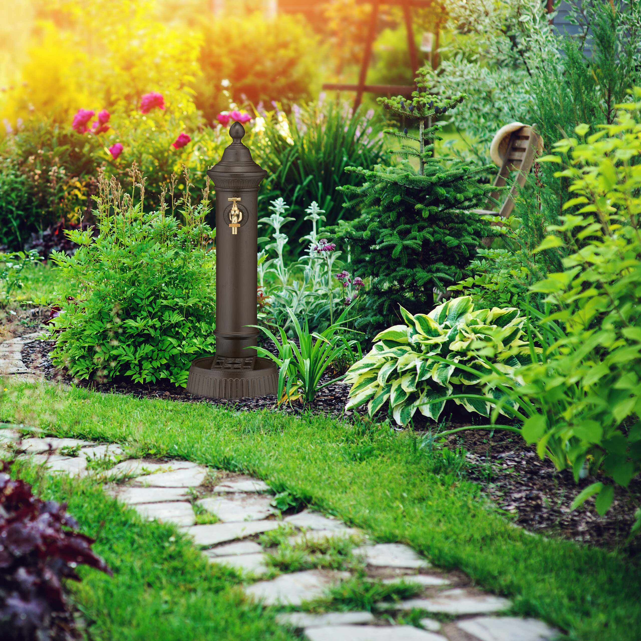 Ein brauner Gartenbrunnen steht aufrecht inmitten von üppigen grünen Pflanzen und Blumen in einem sonnigen Garten.