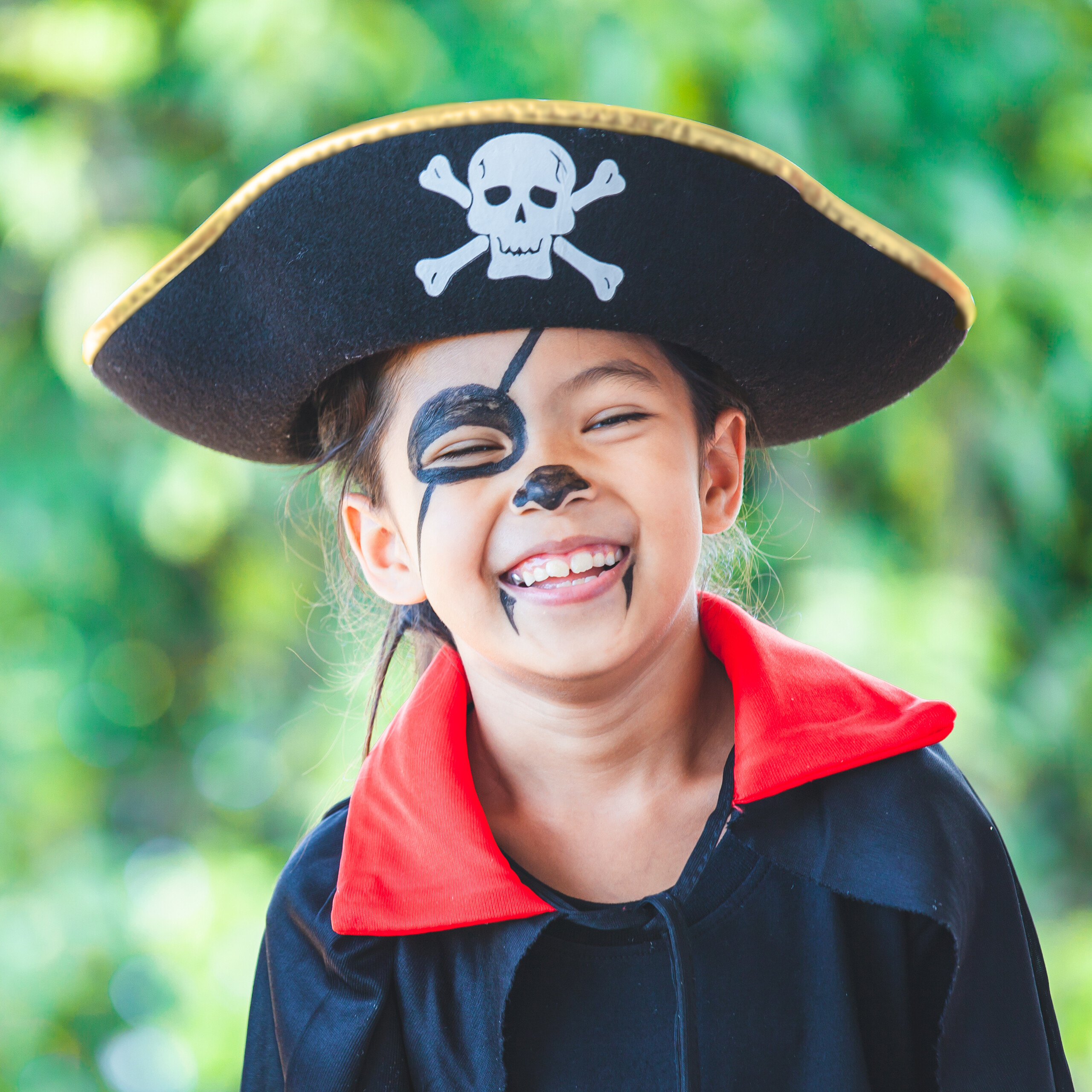 Ein glückliches Mädchen im Piratenkostüm mit Hut und Gesichtsbehaarung lchelt.