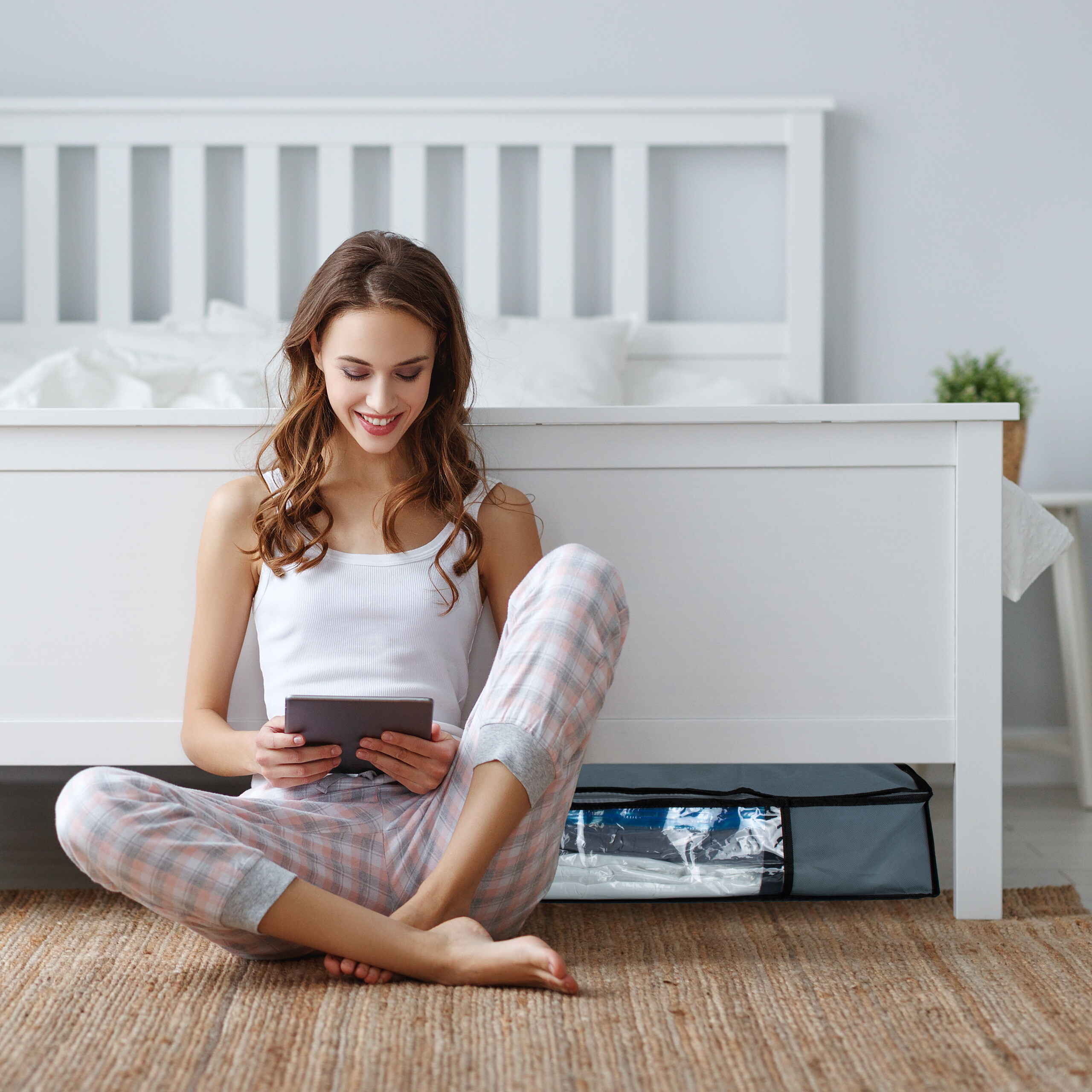 Eine lächelnde Frau in Pyjama sitzt auf dem Teppich im Schlafzimmer und benutzt ein Tablet.