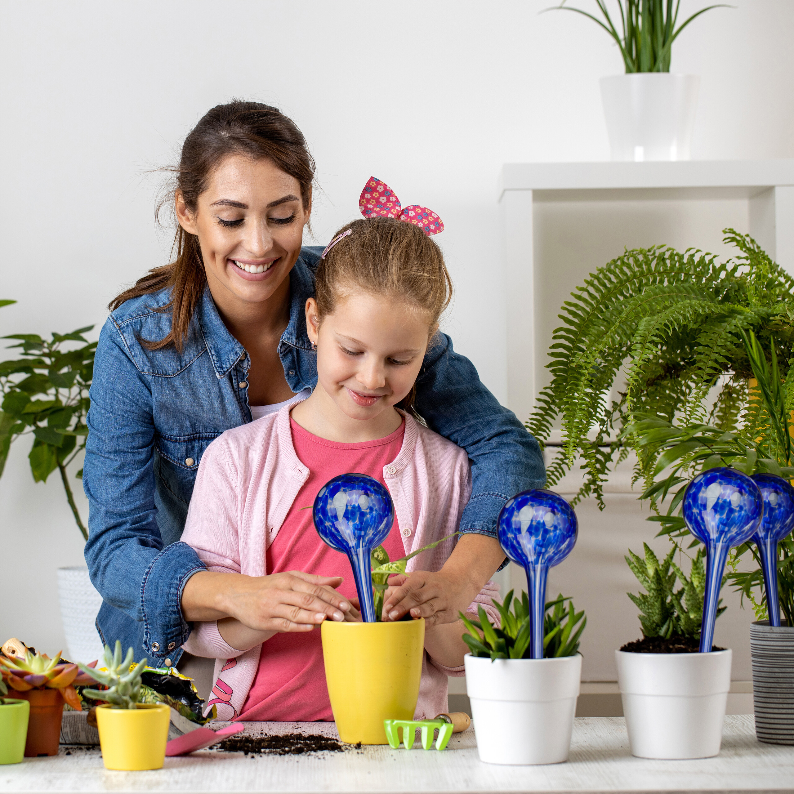 Eine Mutter und Tochter topfen glücklich eine Pflanze ein, umgeben von Zimmerpflanzen.