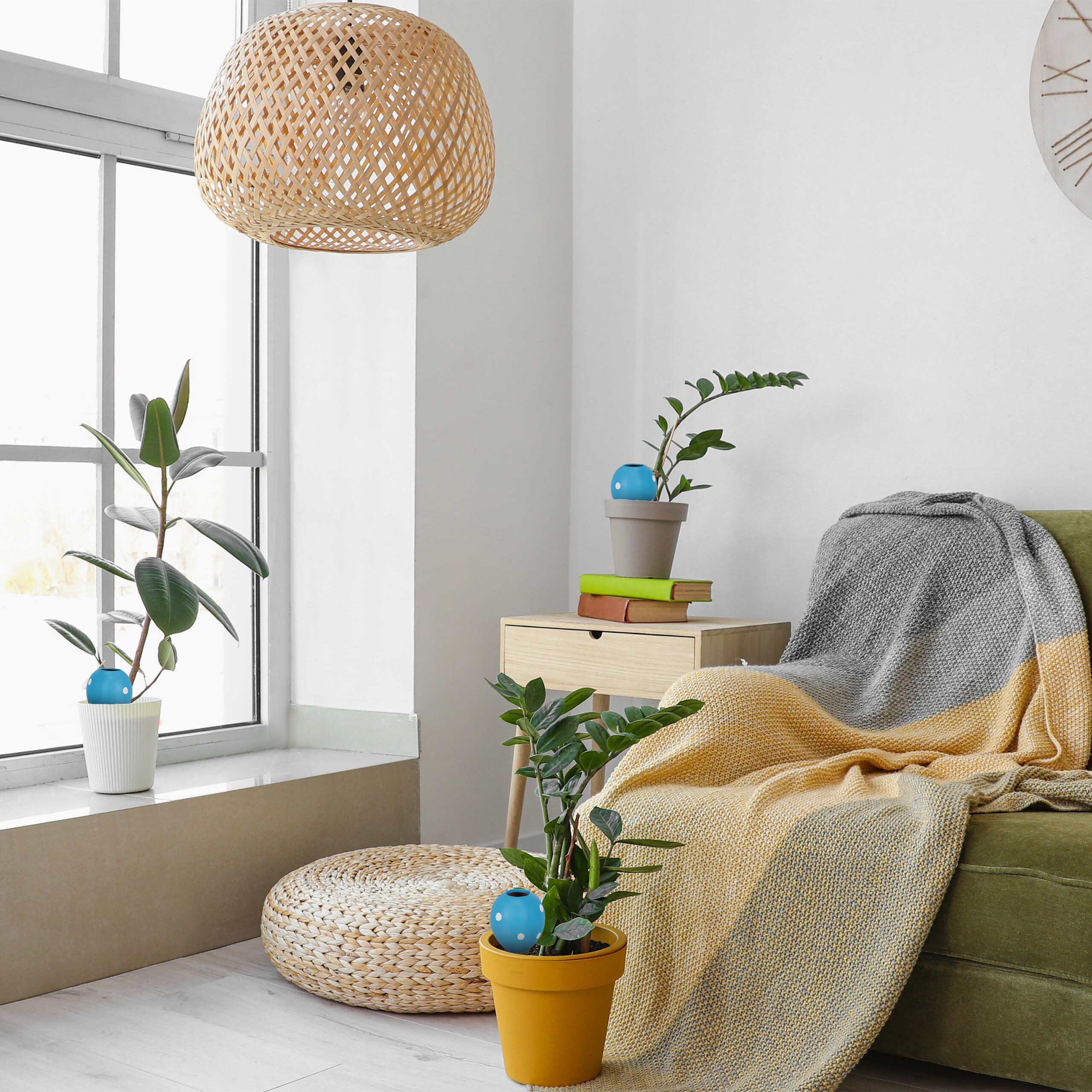 Ein heller Raum mit grünem Sofa, Kissen, Pflanzen in Töpfen, Woven-Lampenschirm und einem großen Fenster.