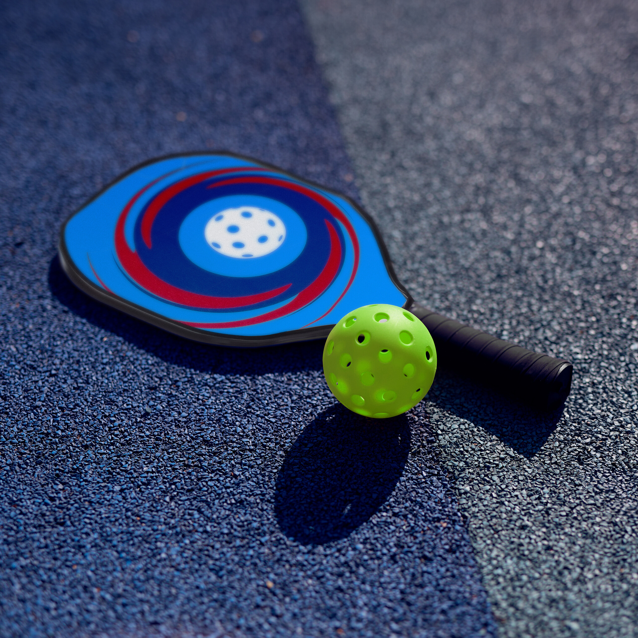 Ein blauer Pickleball-Schläger mit Wirbelmuster und ein gelber Lochball liegen auf einem blauen Sportplatz.