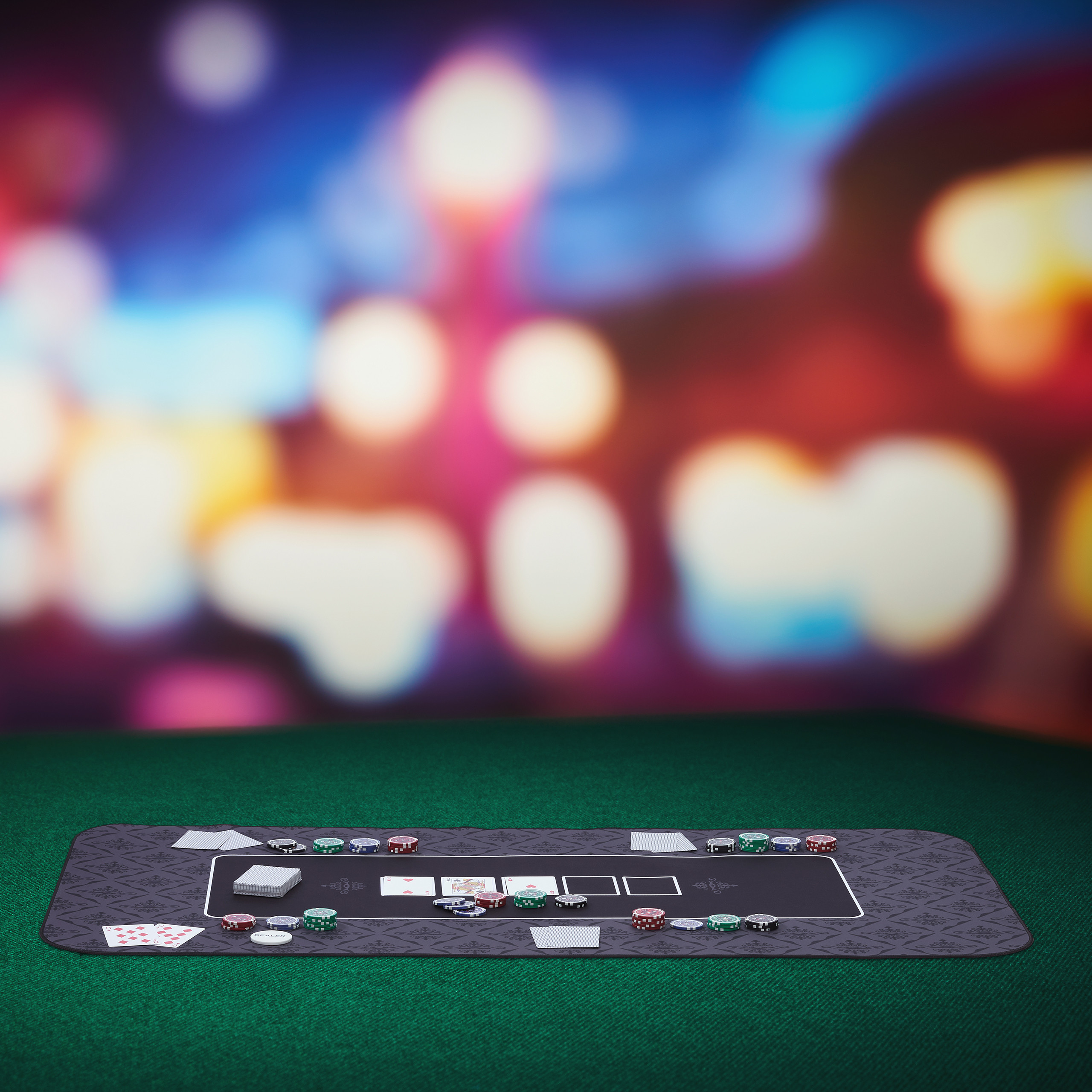 Ein Pokertisch mit Spielkarten und Chips auf grüner Filzoberfläche vor verschwommenem, buntem Hintergrund.