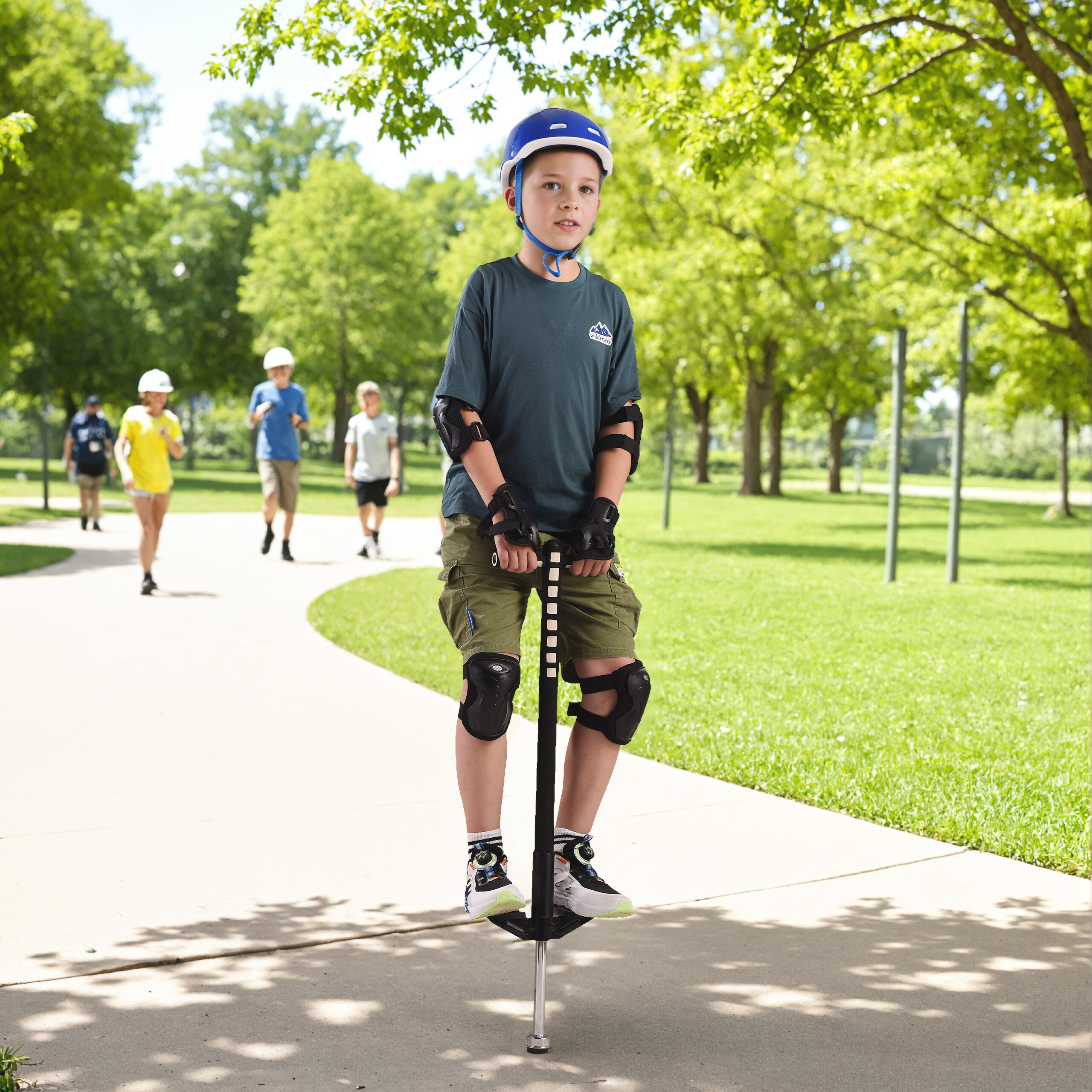 Ein Junge in Schutzkleidung springt auf einem Pogo-Stick im Park; andere Kinder im Hintergrund.