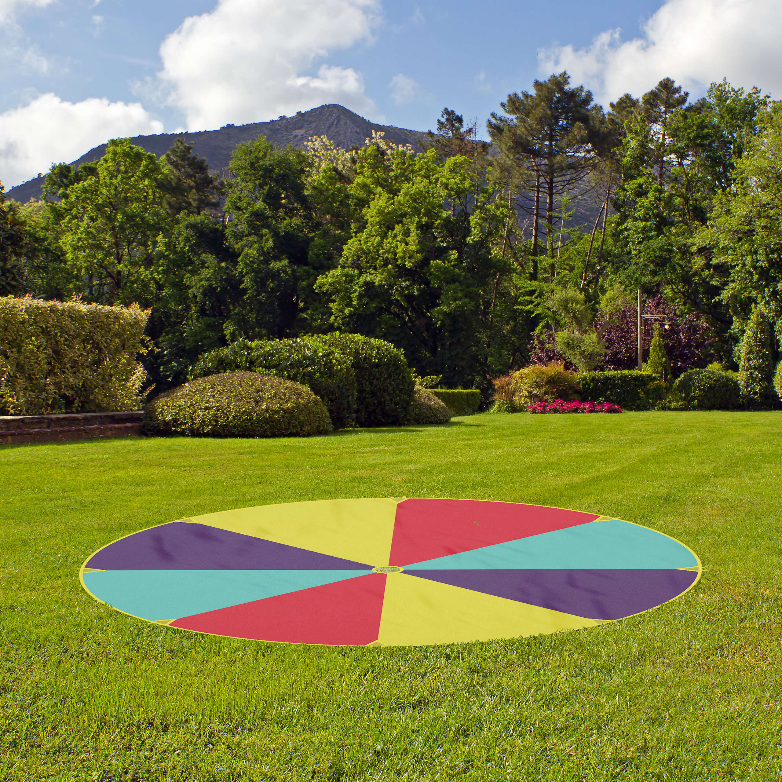 Eine bunte Picknickdecke liegt auf einem grünen Rasen mit Bäumen und einem Berg im Hintergrund.