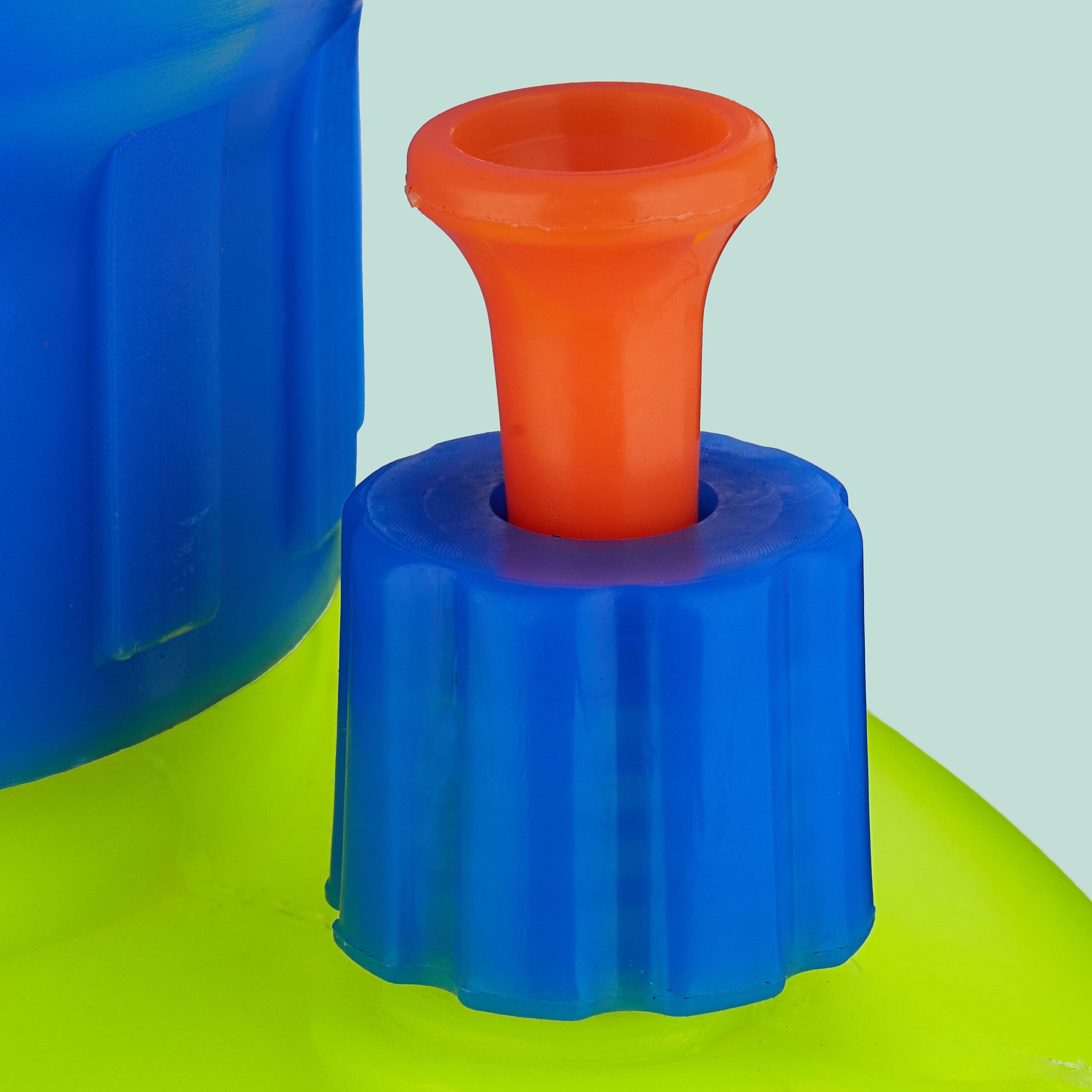 Ein orangefarbenes Düsenstück ragt aus einer blauen Kappe auf einem hellgrünen Behälter.