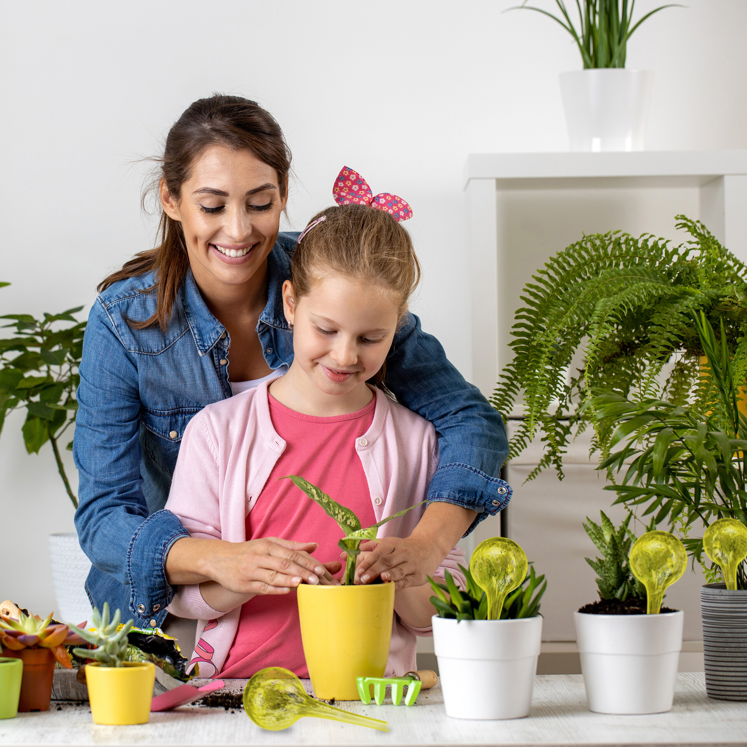 Eine lächelnde Mutter und Tochter pflanzen einen kleinen grünen Trieb in einen gelben Topf.