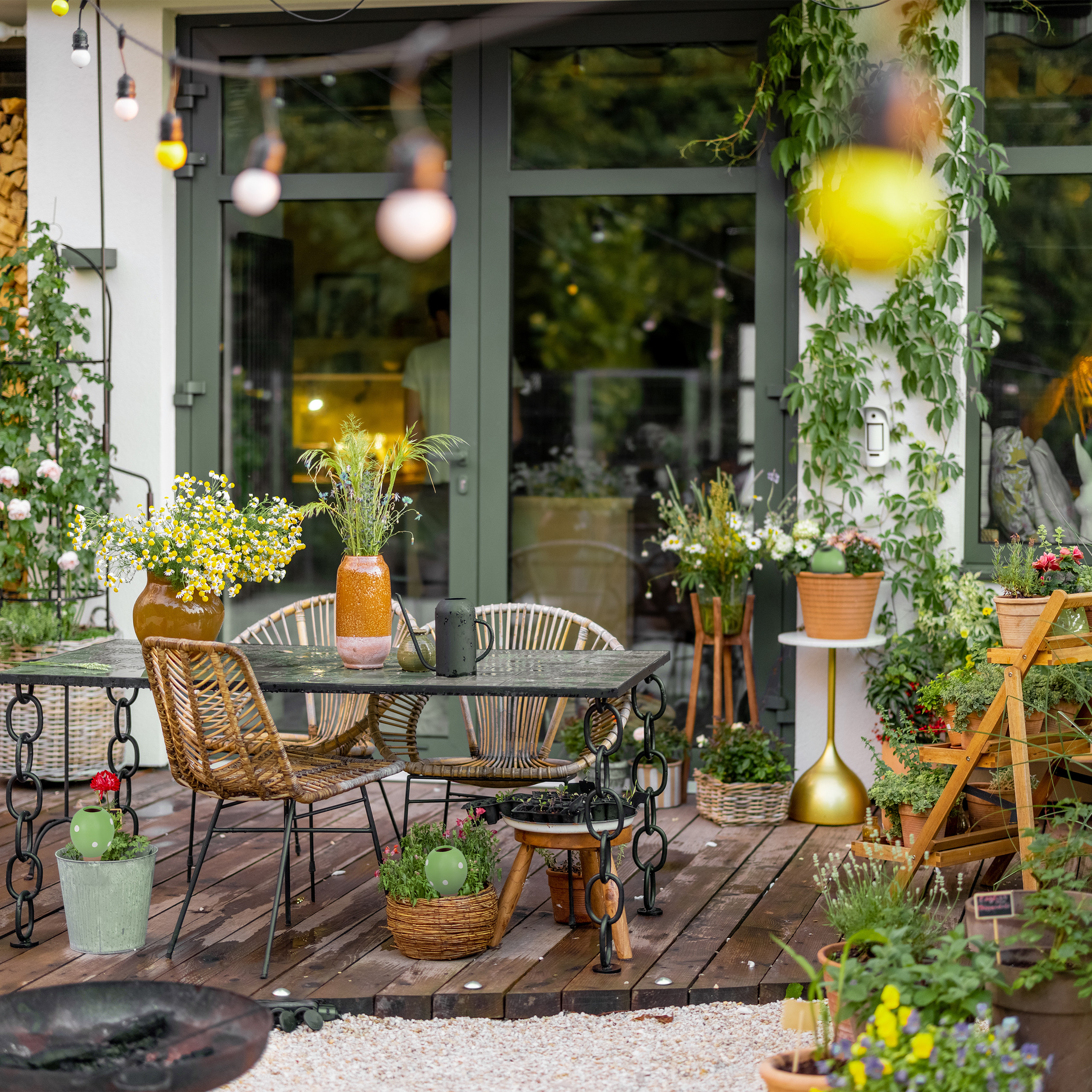 Eine gemütliche Terrasse mit Holzboden, Esstisch, Rattanstühlen und vielen Blumen in Töpfen und Vasen.