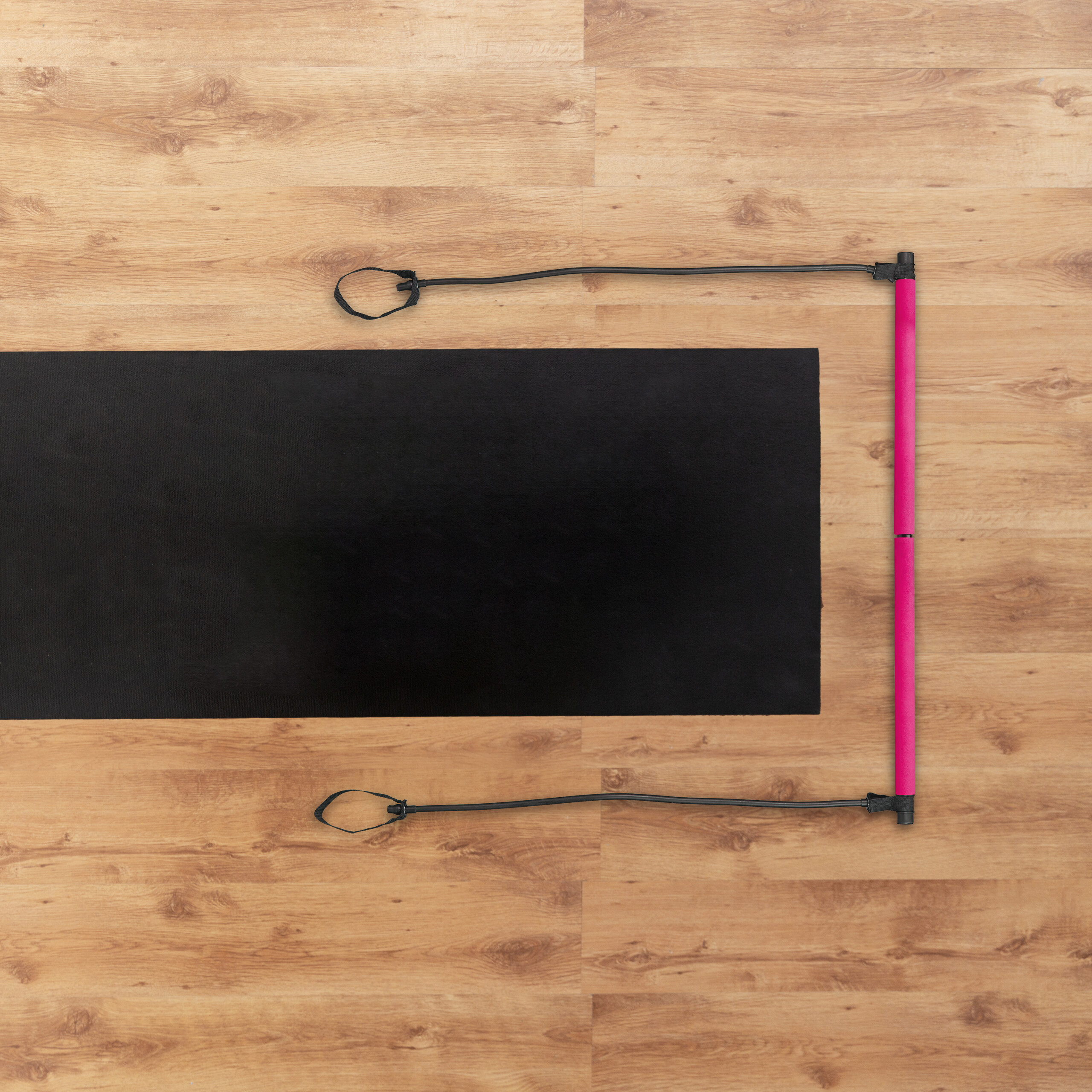 Eine schwarze Gymnastikmatte und ein pinkes Widerstandsband auf einem Holzboden.