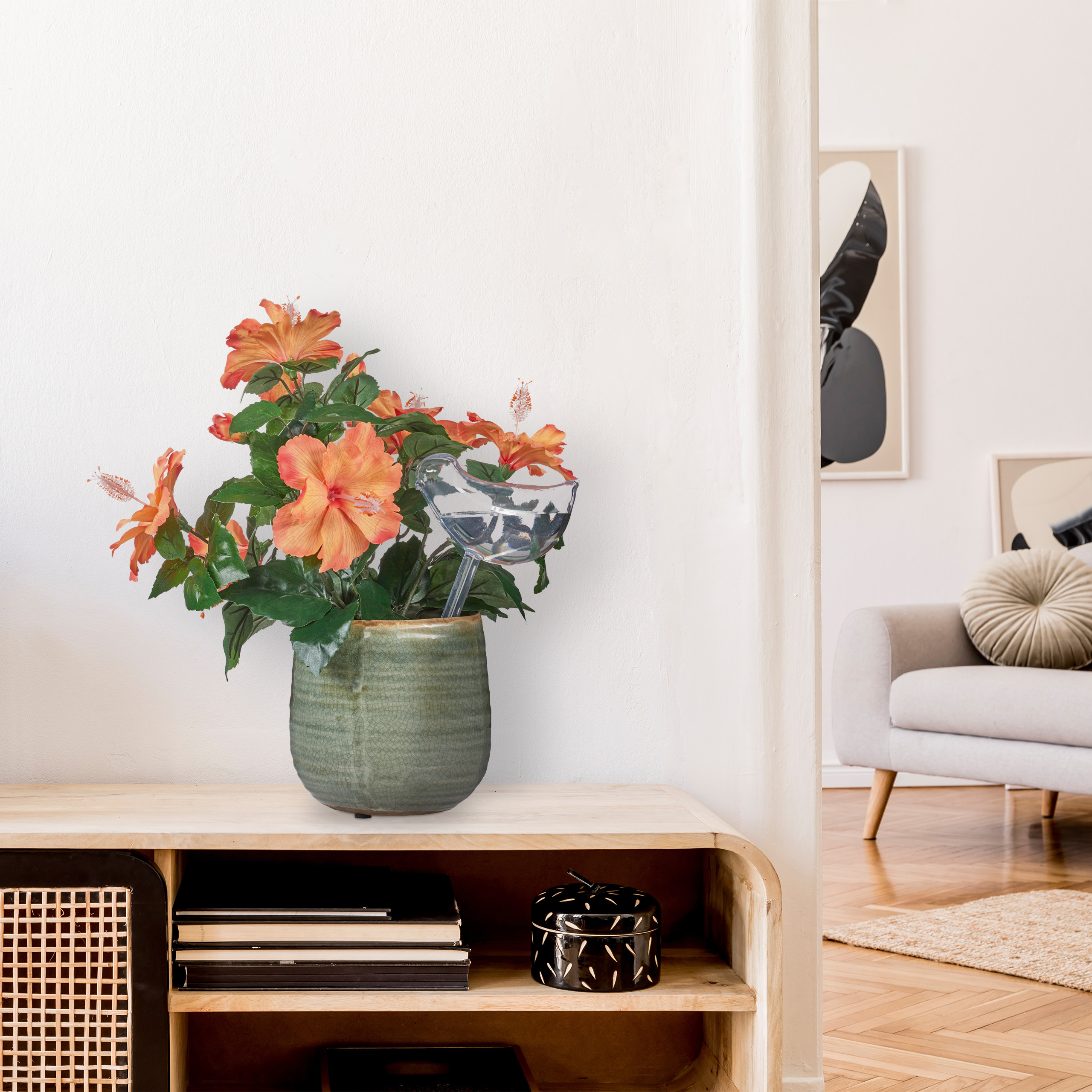 Eine grüne Vase mit orangefarbenen Blumen steht auf einer Holzkommode, im Hintergrund ist ein helles Zimmer zu sehen.