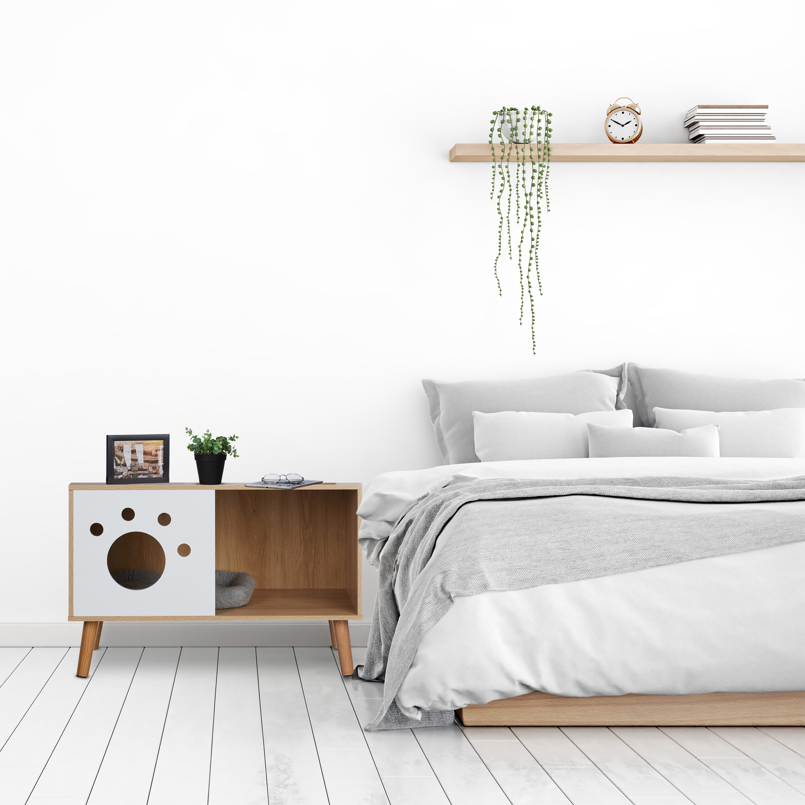 Ein modernes Schlafzimmer mit weißem Bett, Nachttisch mit Katzenhaus und Wandregal mit Büchern.
