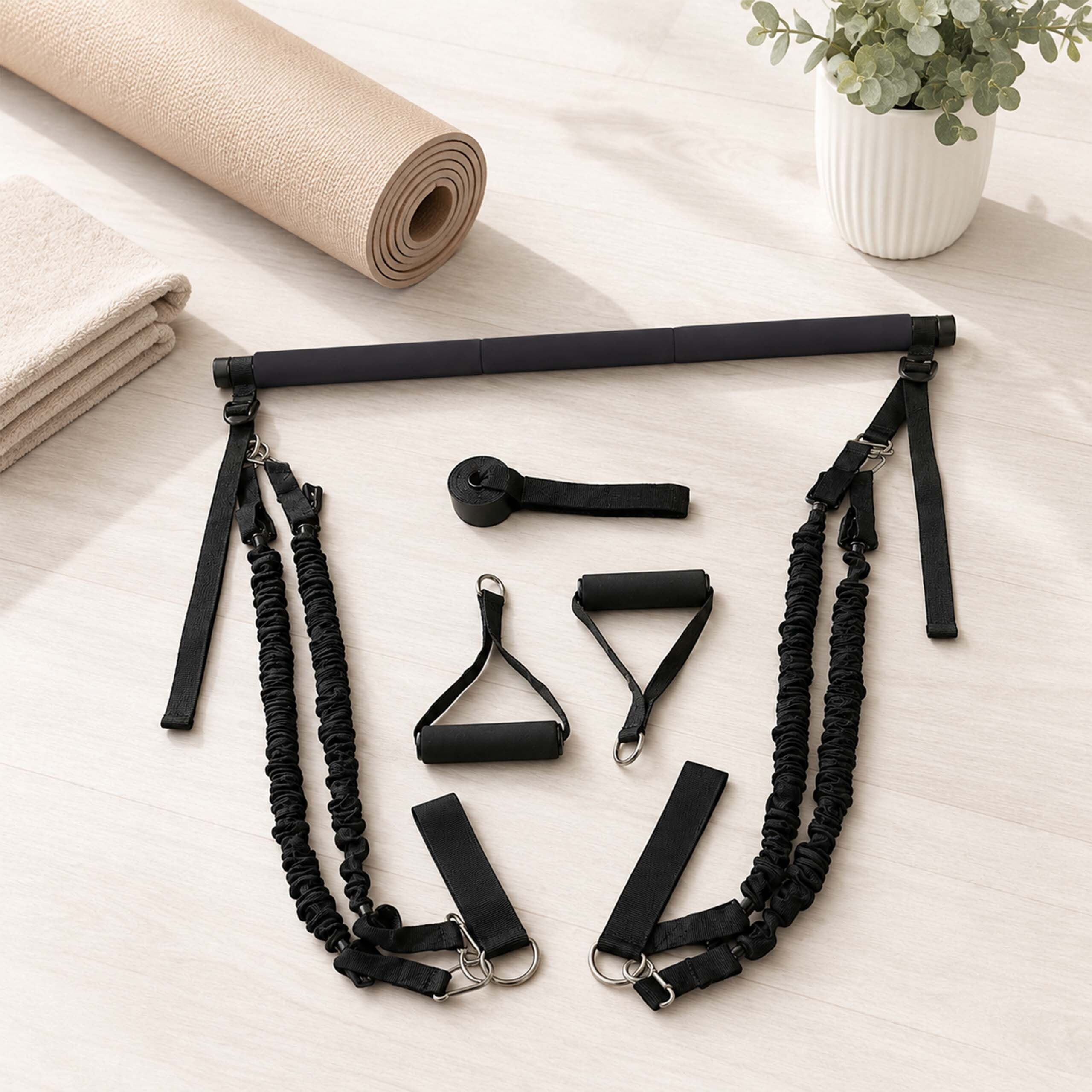 Schwarzes Pilates-Stangenset mit Widerstandsbändern, Yoga-Matte, Handtuch und Pflanze auf hellem Holzboden.