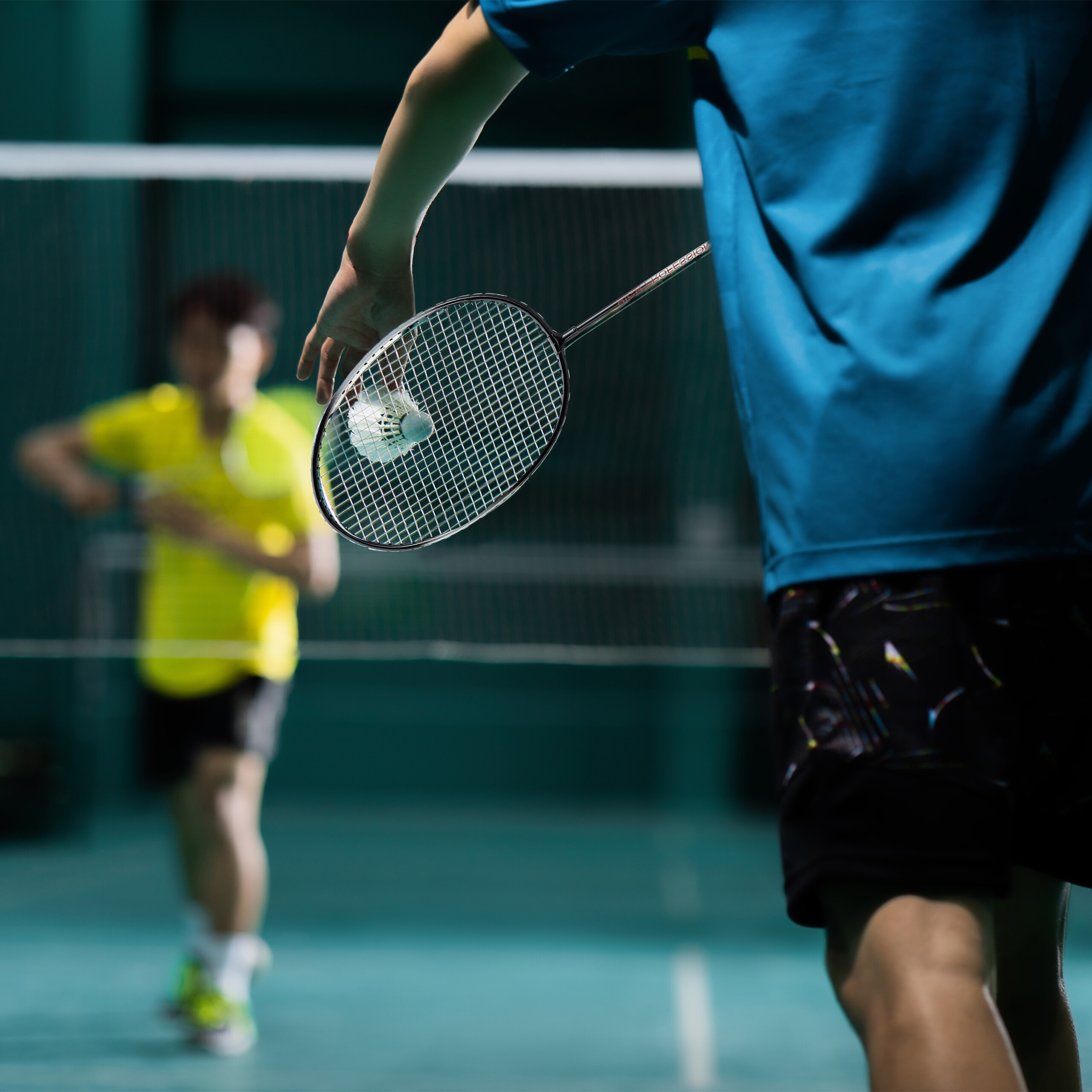 Ein Badmintonspieler in Blau hält einen Schläger mit einem Federball in der Nähe des Netzes.