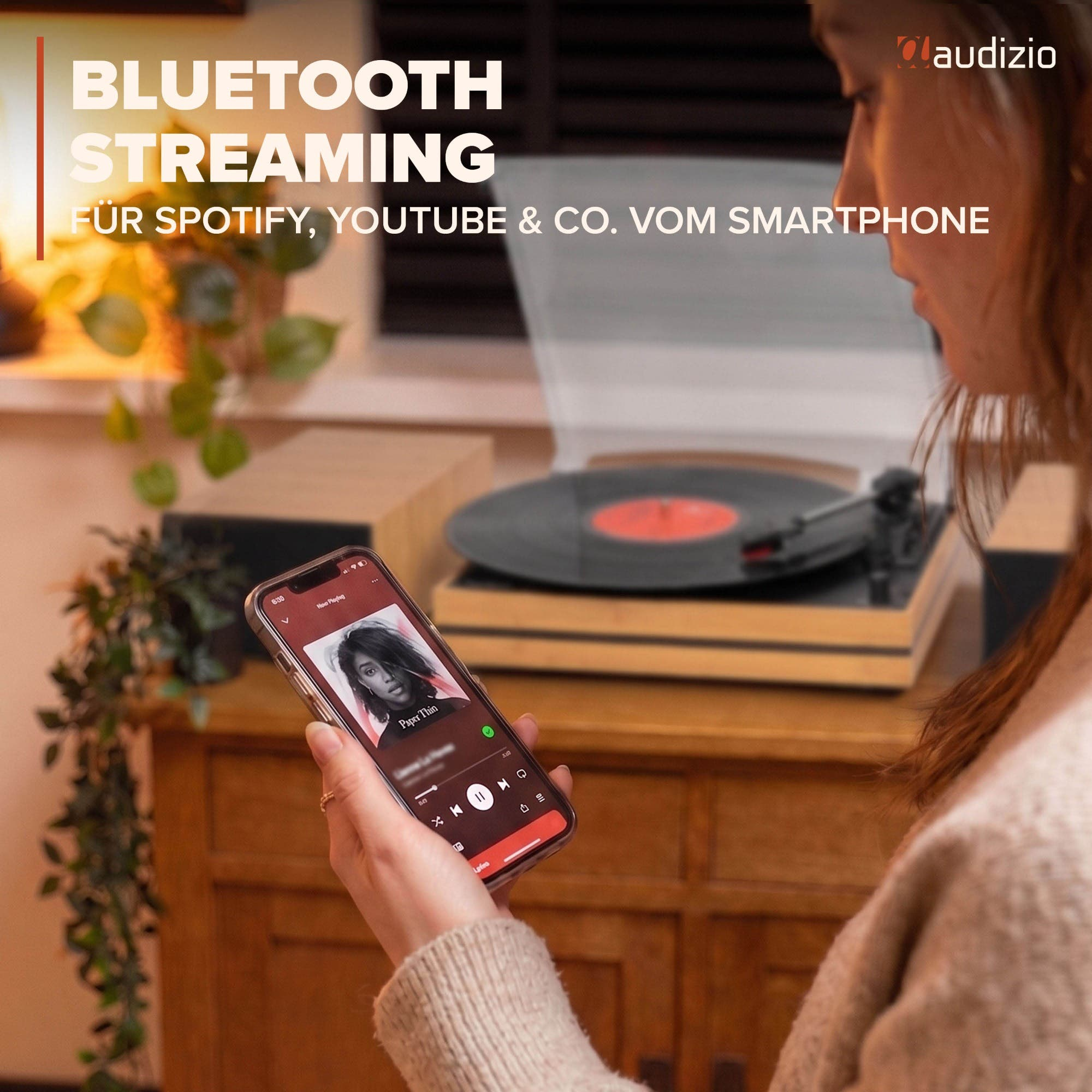 Una mujer usa una aplicación de música en su teléfono con un tocadiscos reproduciendo de fondo.