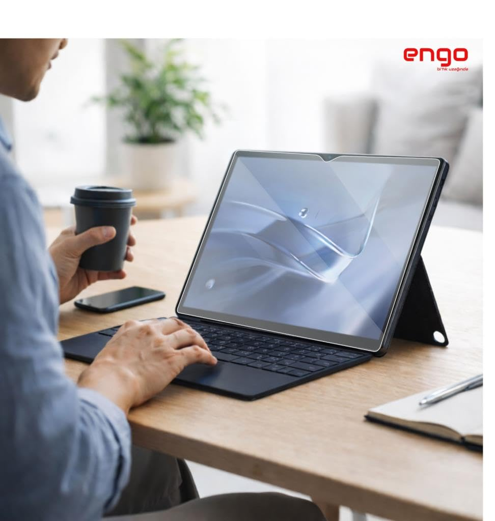 Ahşap bir masada klavyeli tablet kullanan, elinde kahve bardağı tutan bir kişi.