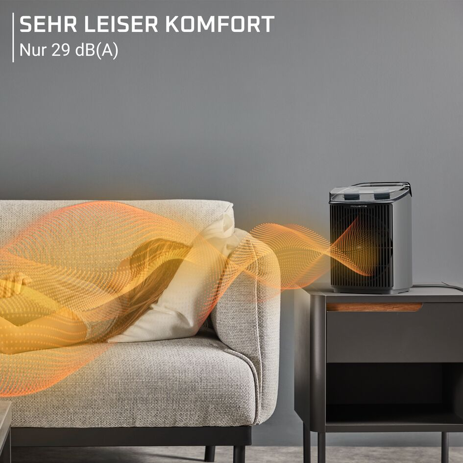 Un termoventilatore nero su un comodino accanto a un divano dove una donna dorme pacificamente.