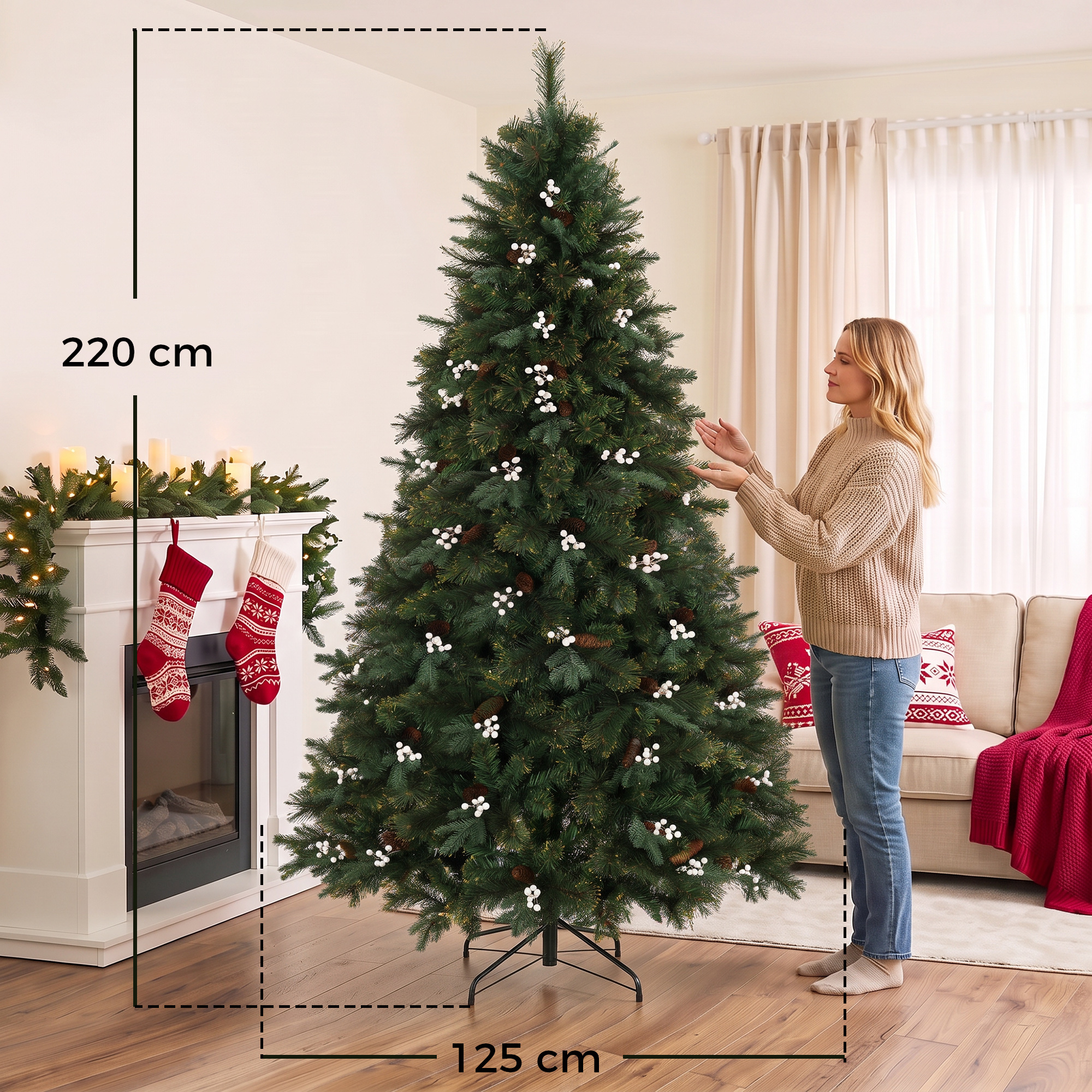 Una mujer rubia está de pie junto a un árbol de Navidad de 220 cm decorado con bayas blancas y piñas en una sala.