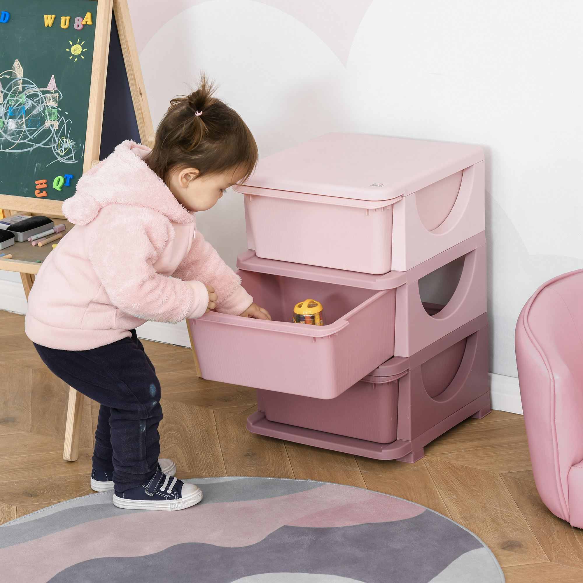 Un niño abre una caja de almacenamiento de juguetes rosa junto a una pizarra verde.