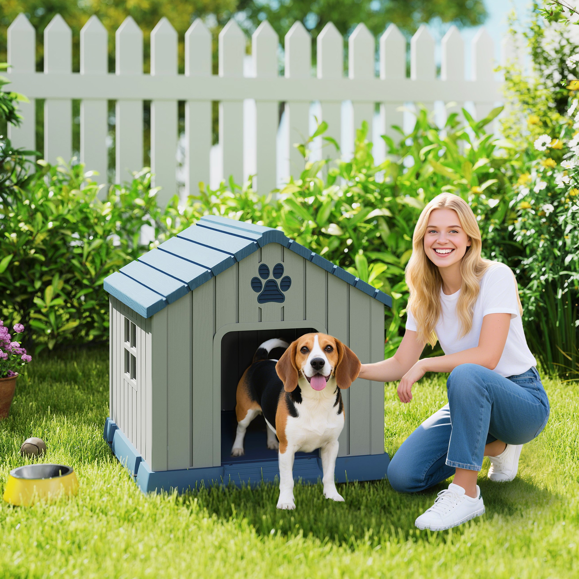 Una mujer sonriente se arrodilla junto a una caseta gris con un beagle adentro, en un jardín verde.