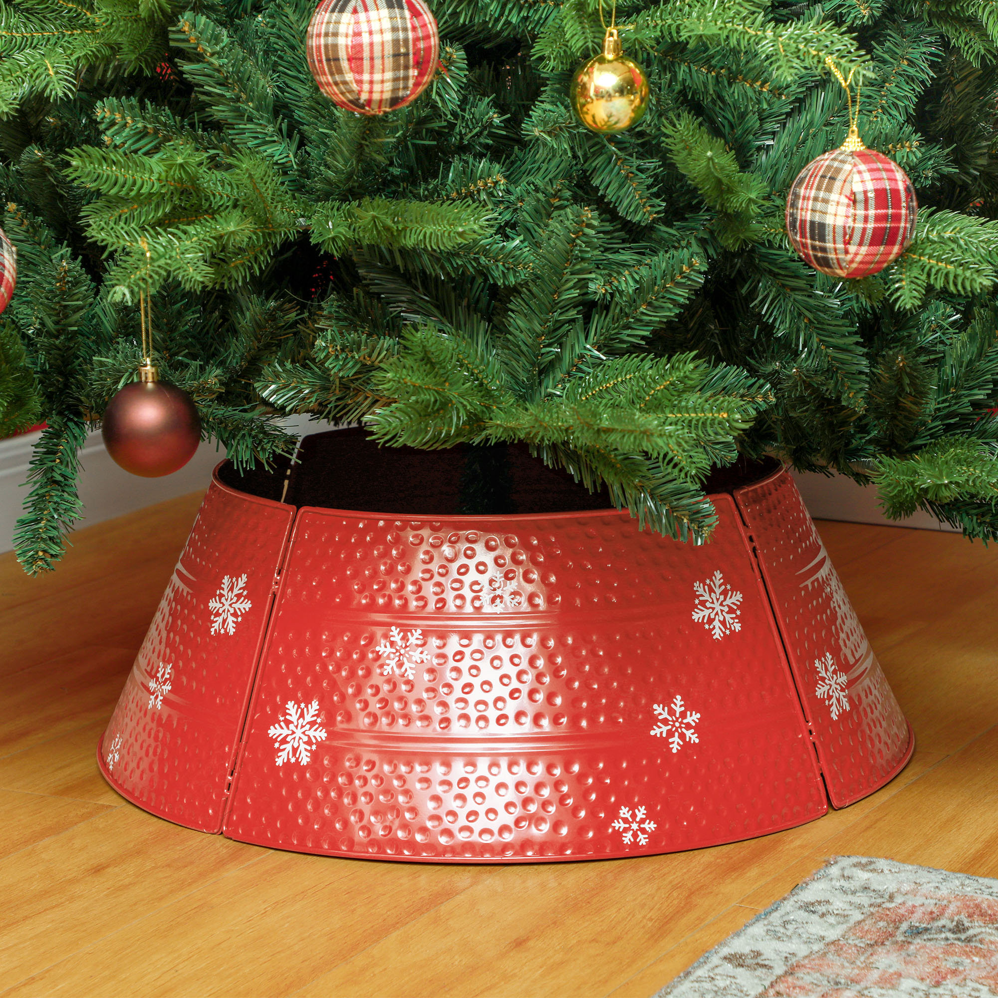 Un collar de metal rojo para árbol de Navidad con copos de nieve blancos se encuentra en la base de un árbol.