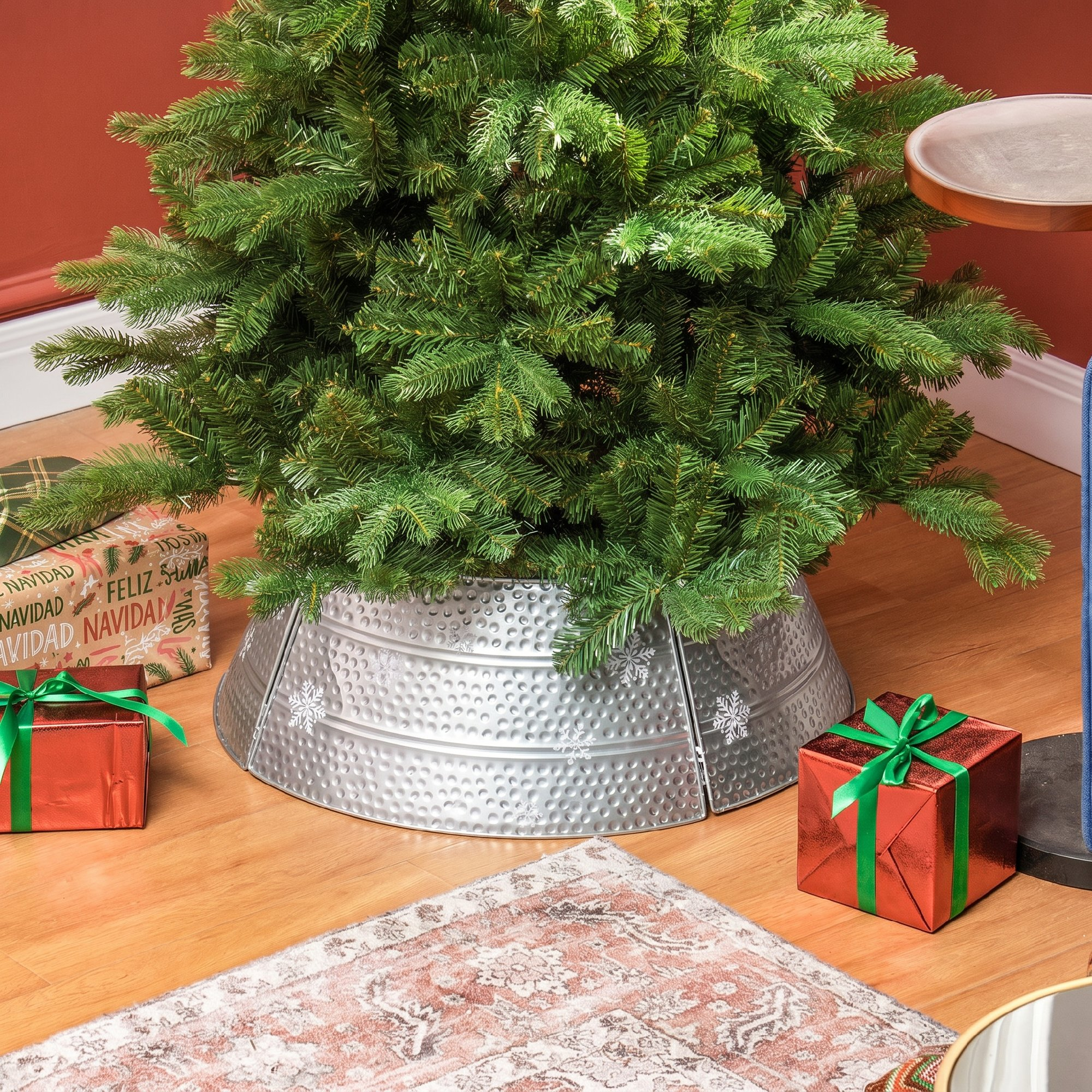 Un árbol de Navidad decorado con soporte de metal plateado, regalos envueltos y una alfombra en el piso.