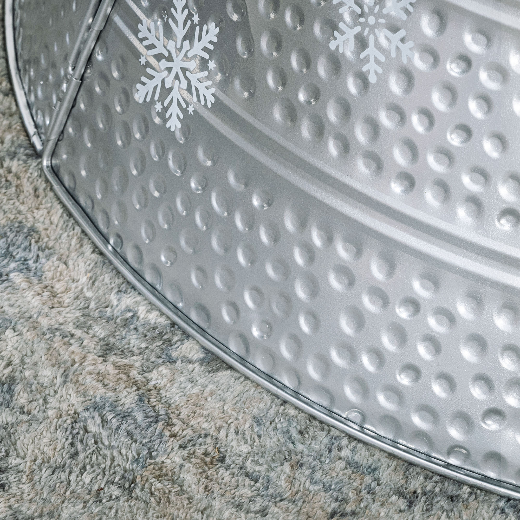 Una tina de metal plateada con hoyuelos y copos de nieve blancos sobre una alfombra gris.