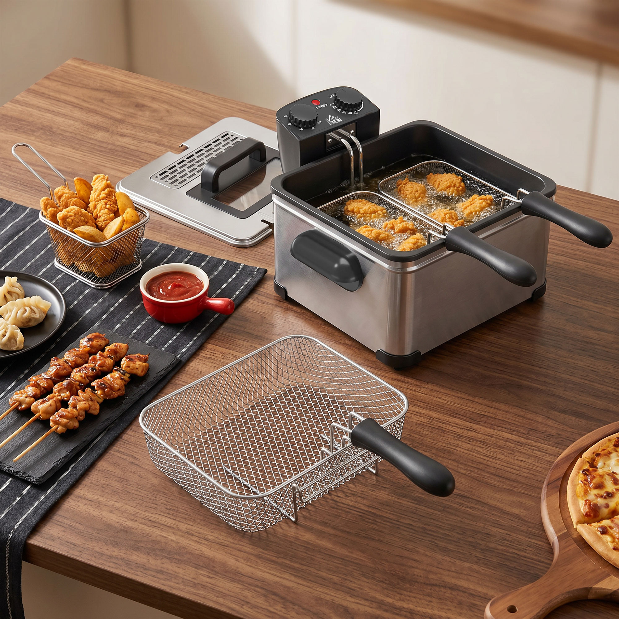 Una freidora de acero inoxidable en una mesa de madera con pollo frito, brochetas y pizza.