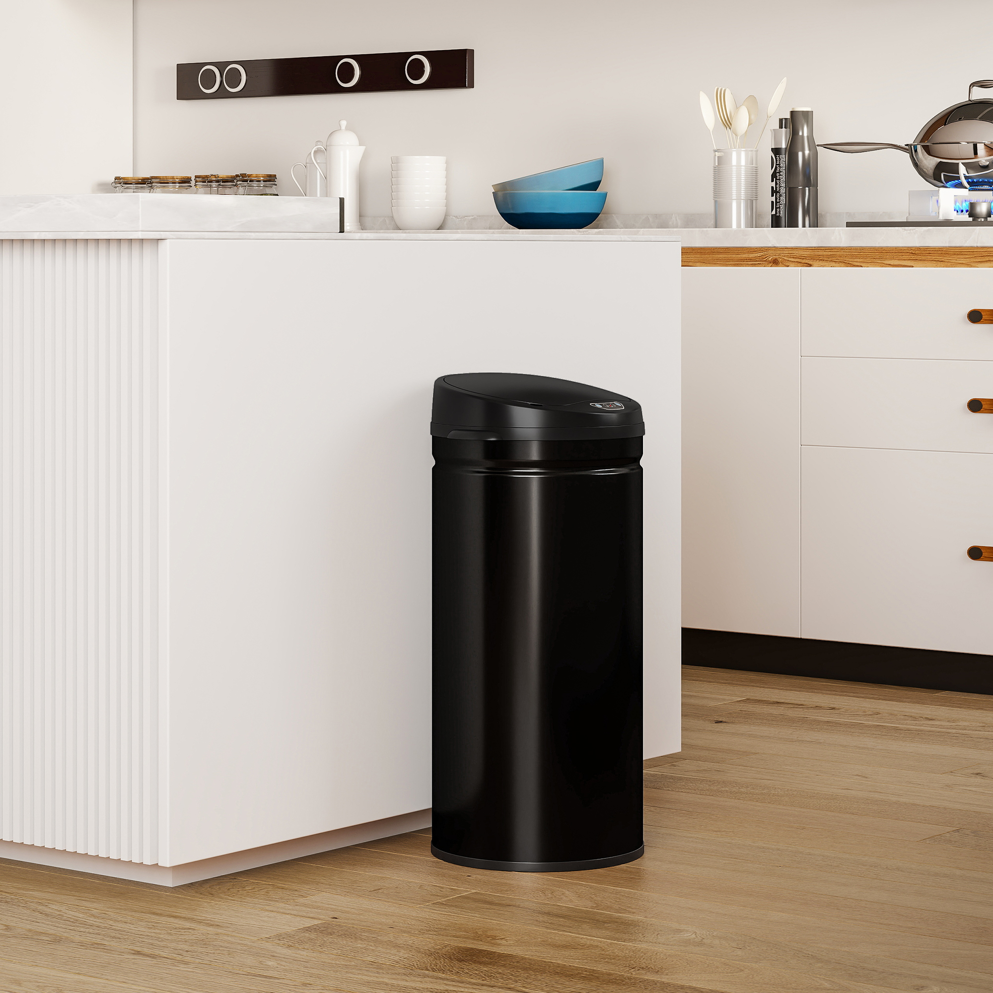 Un bote de basura negro con tapa automática se encuentra en una cocina moderna frente a una isla de cocina blanca.