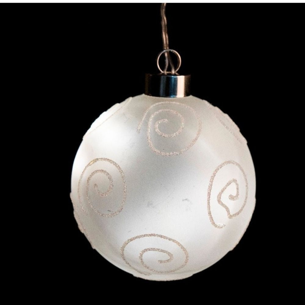 Un adorno navideño blanco con espirales brillantes sobre un fondo negro.