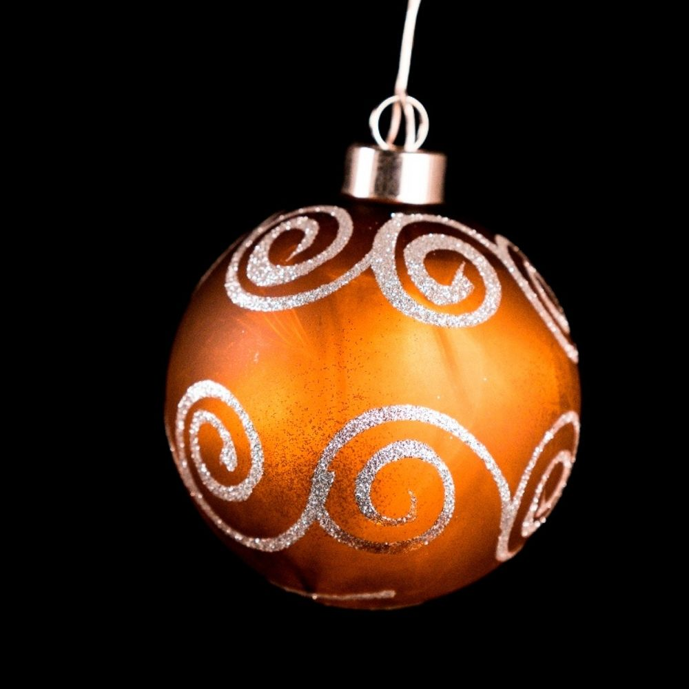 Bola de navidad naranja brillante con motivos de espiral de purpurina plateada sobre fondo negro.