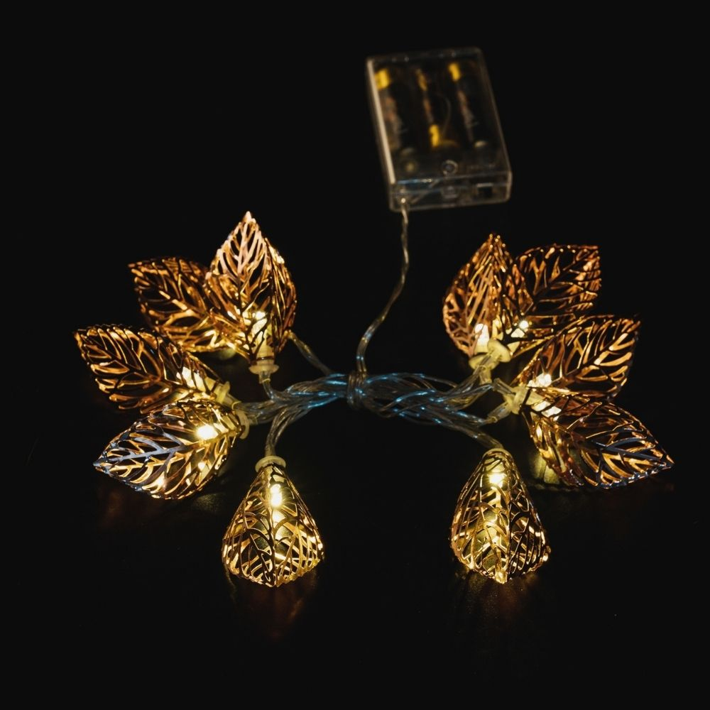 Luces de hadas doradas en forma de hoja brillan sobre un fondo oscuro, conectadas a un portapilas.