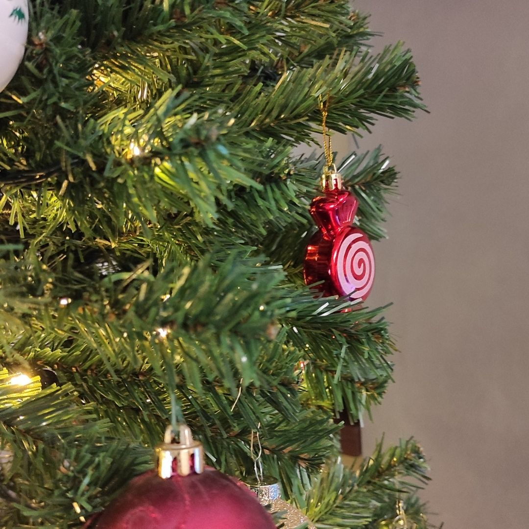 Un árbol de Navidad decorado con adornos de caramelos y esferas rojas junto a luces cálidas.