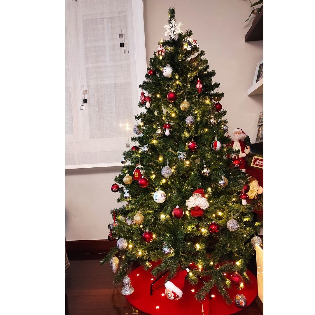 Un árbol de Navidad decorado con luces, esferas rojas y plateadas, una figura de Papá Noel y una falda roja.