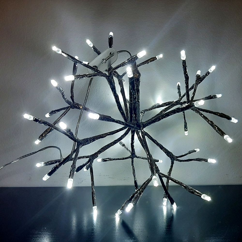 Una estructura de rama oscura decorativa con luces LED blancas parpadeantes en una mesa oscura contra una pared gris.