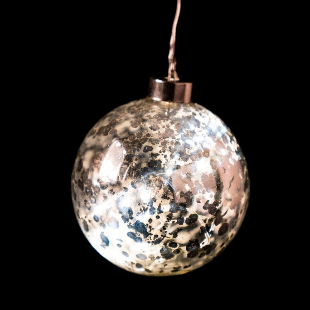 Una bola de Navidad brillante y moteada cuelga de un alambre fino sobre un fondo oscuro.
