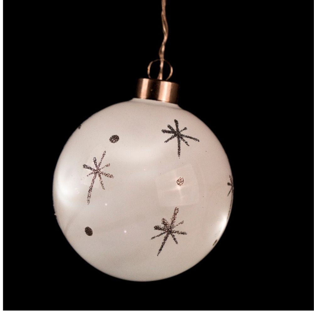 Una bola de Navidad blanca decorada con estrellas brillantes cuelga sobre un fondo negro.