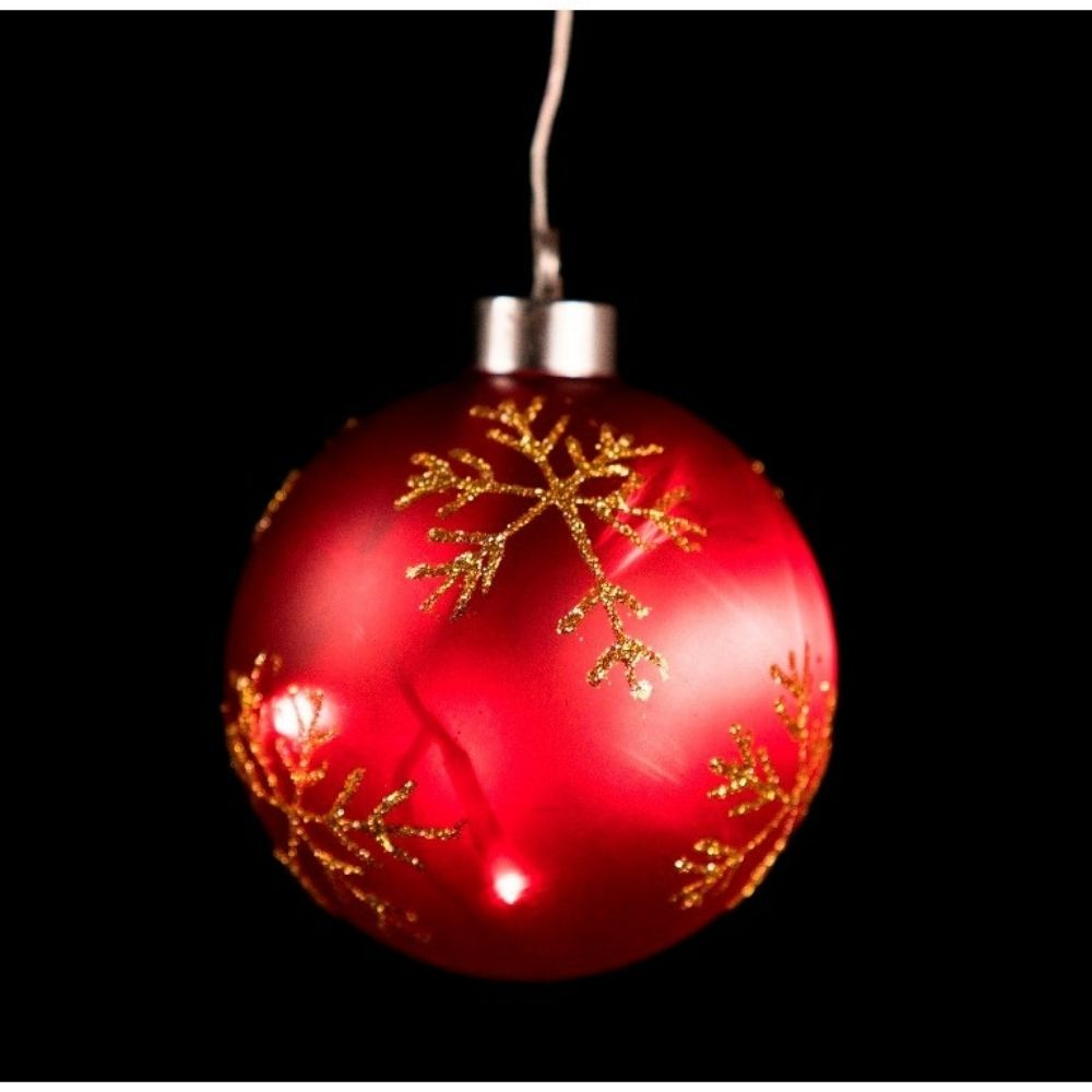Una bola de Navidad roja con copos de oro cuelga de un hilo sobre un fondo negro.