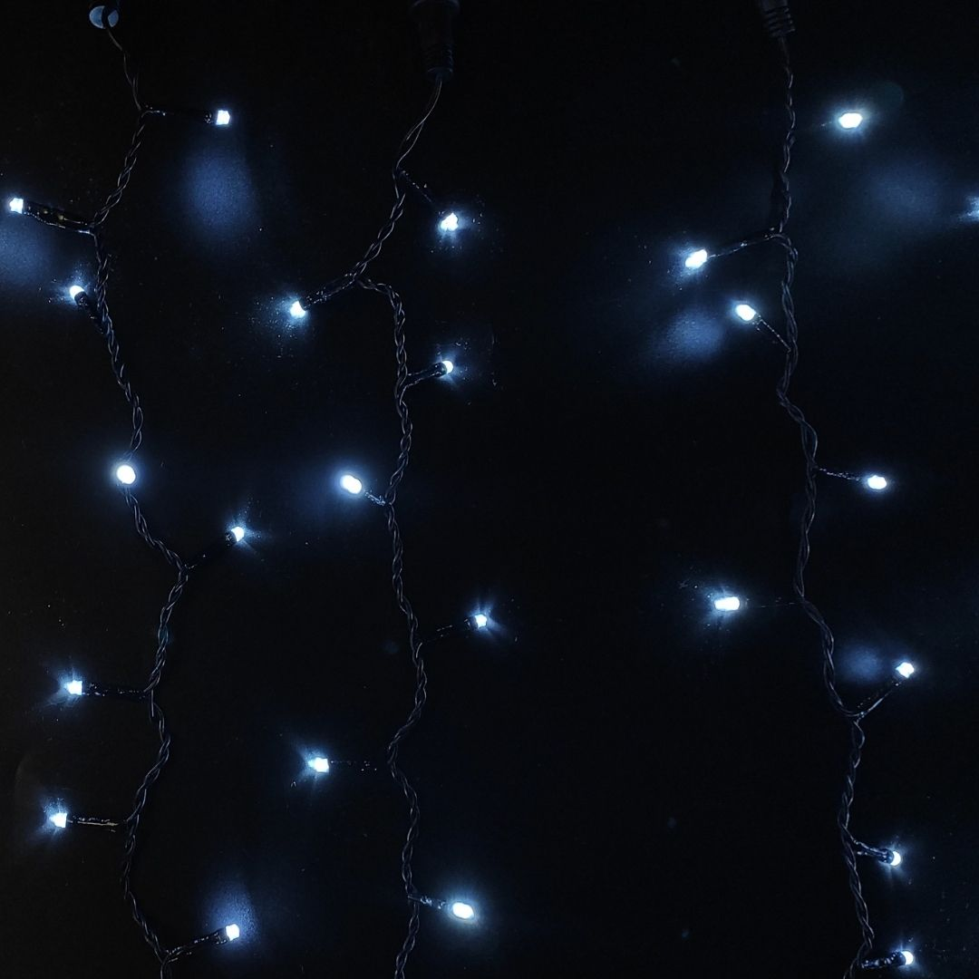 Luces de hadas blancas brillantes cuelgan verticalmente sobre un fondo oscuro.