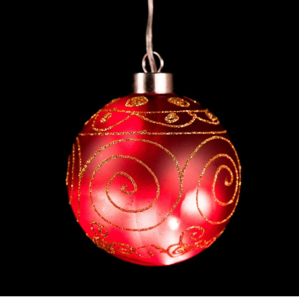Adorno navideño rojo brillante con patrones de remolinos dorados sobre fondo negro.