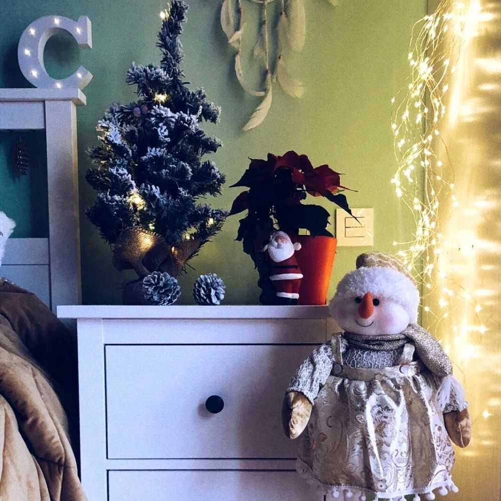 Decoración navideña con árbol nevado, Papá Noel y muñeco de nieve de peluche en una mesa.