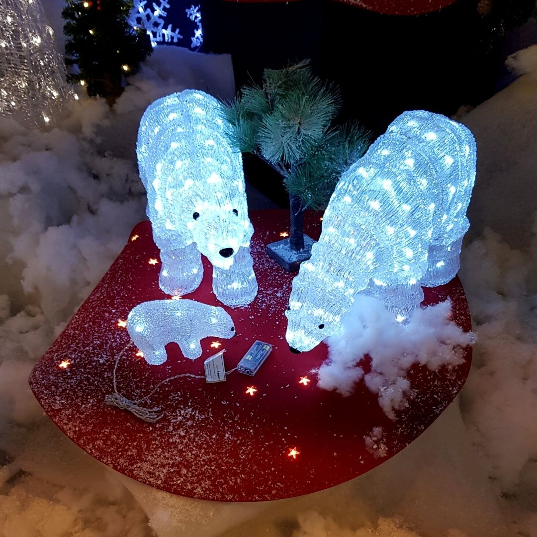 Tres figuras de osos polares iluminados sobre una base roja rodeados de nieve artificial y un pino.