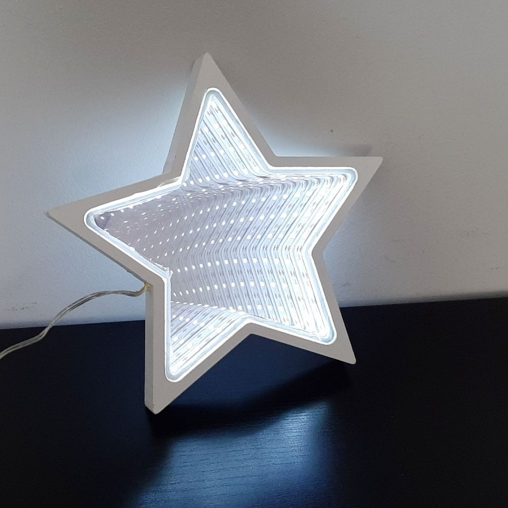 Una lámpara de estrella brillante con efecto de espejo infinito se encuentra en una mesa oscura contra una pared clara.