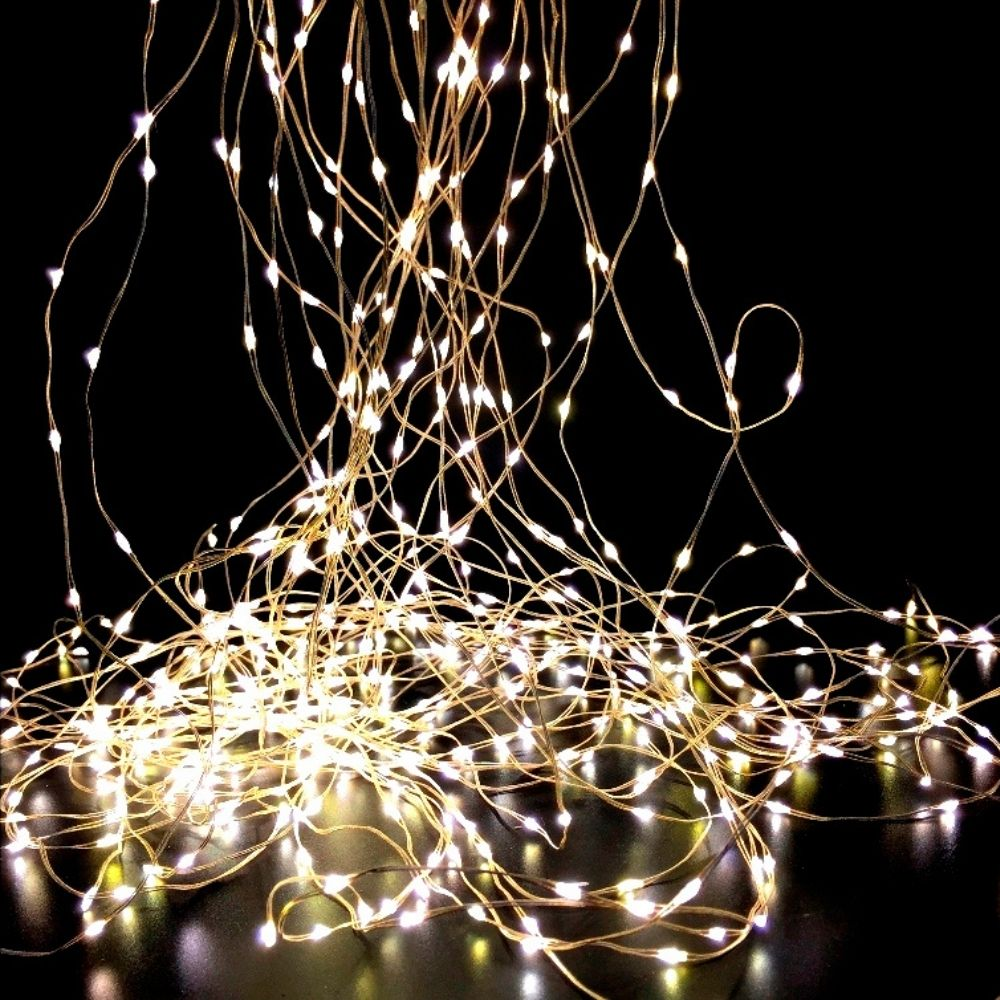 Hilos enredados de luces blancas cálidas brillan sobre un fondo negro sólido, cayendo en cascada sobre una superficie oscura.
